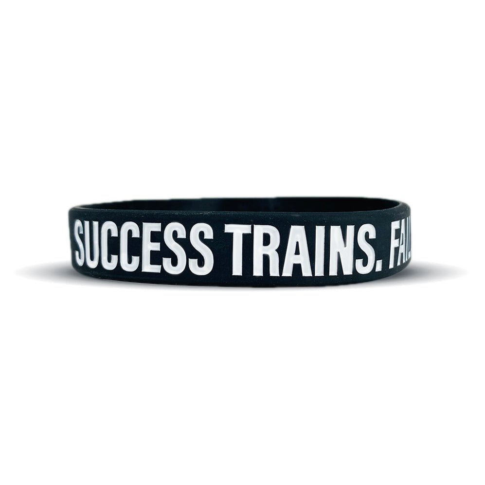 Black wristband with white text 'SUCCESS TRAINS. FAIL' on a white background