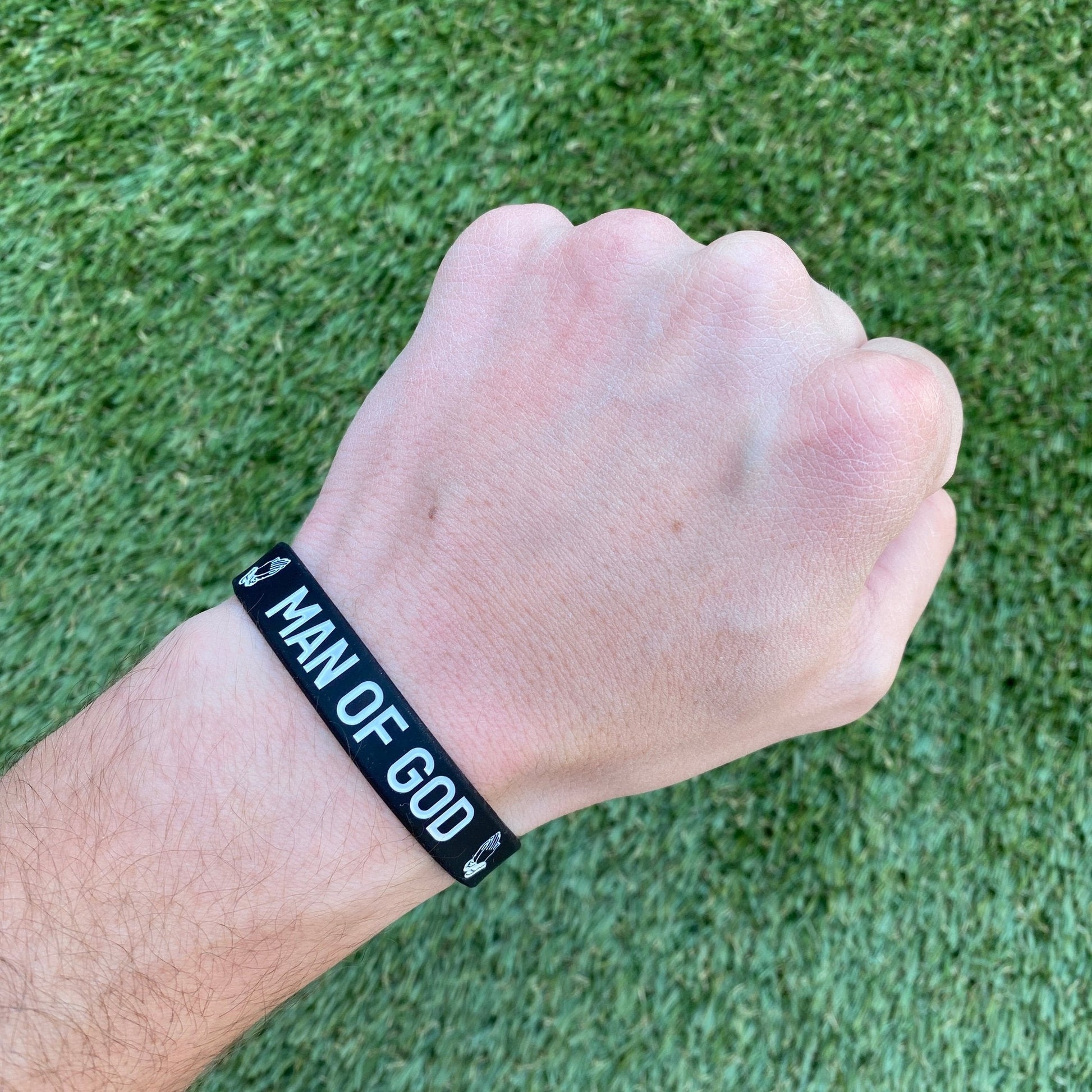 Hand wearing a black wristband with 'Man of God' text on a grass background