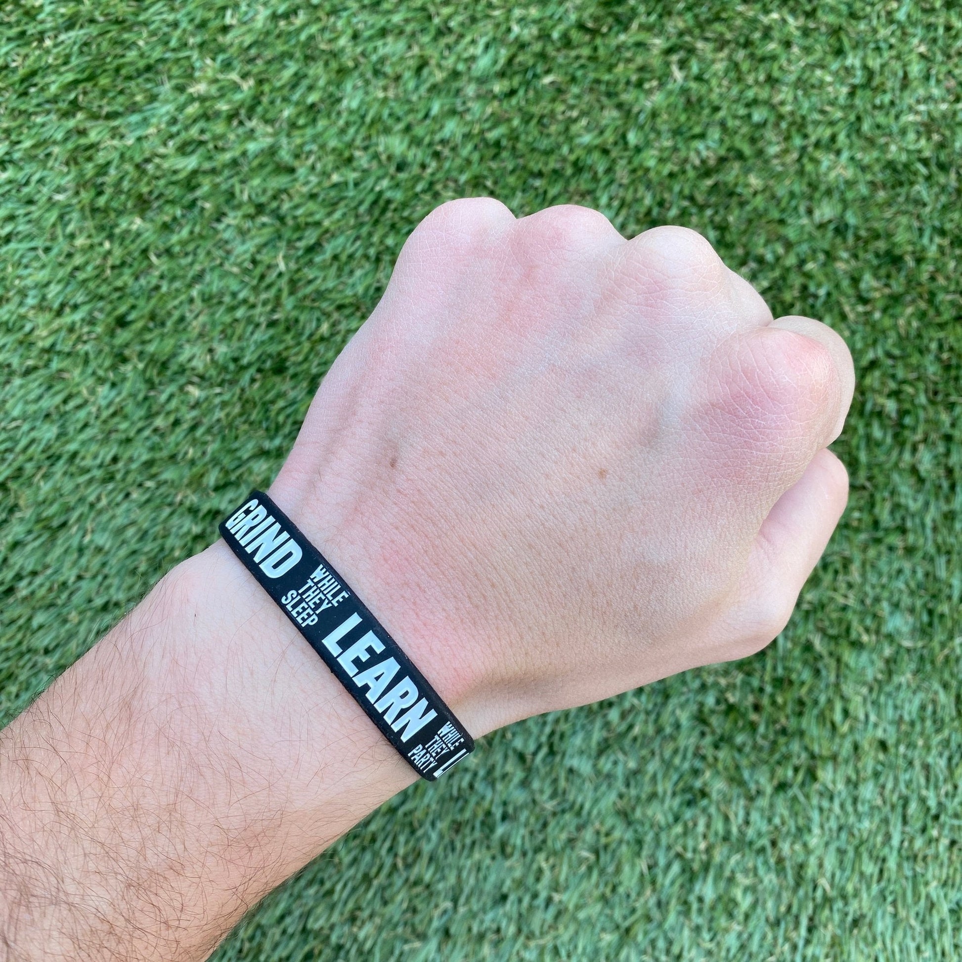 Hand wearing a black wristband with text on a grass background