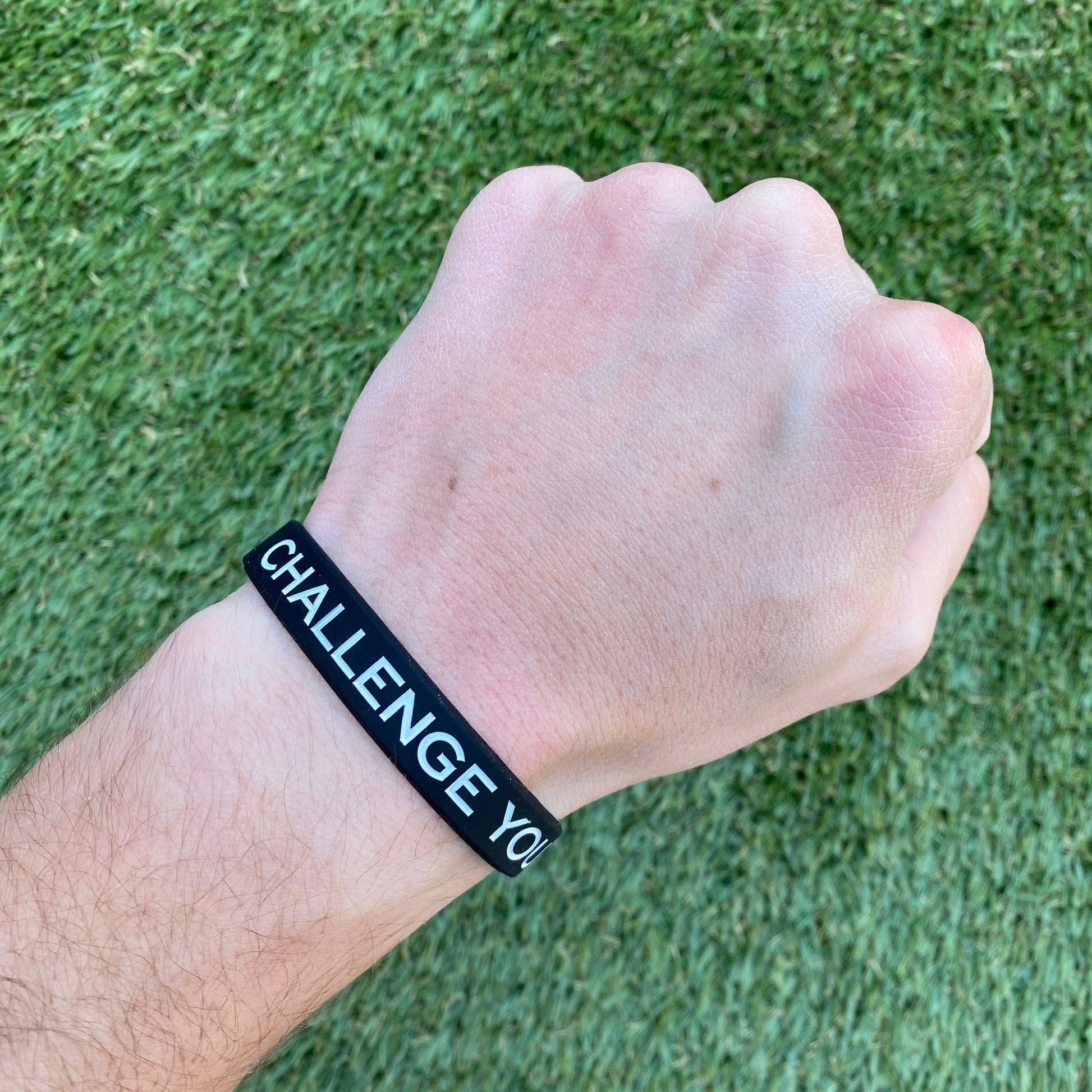Hand wearing a black wristband with 'CHALLENGE YOU' text on a grass background