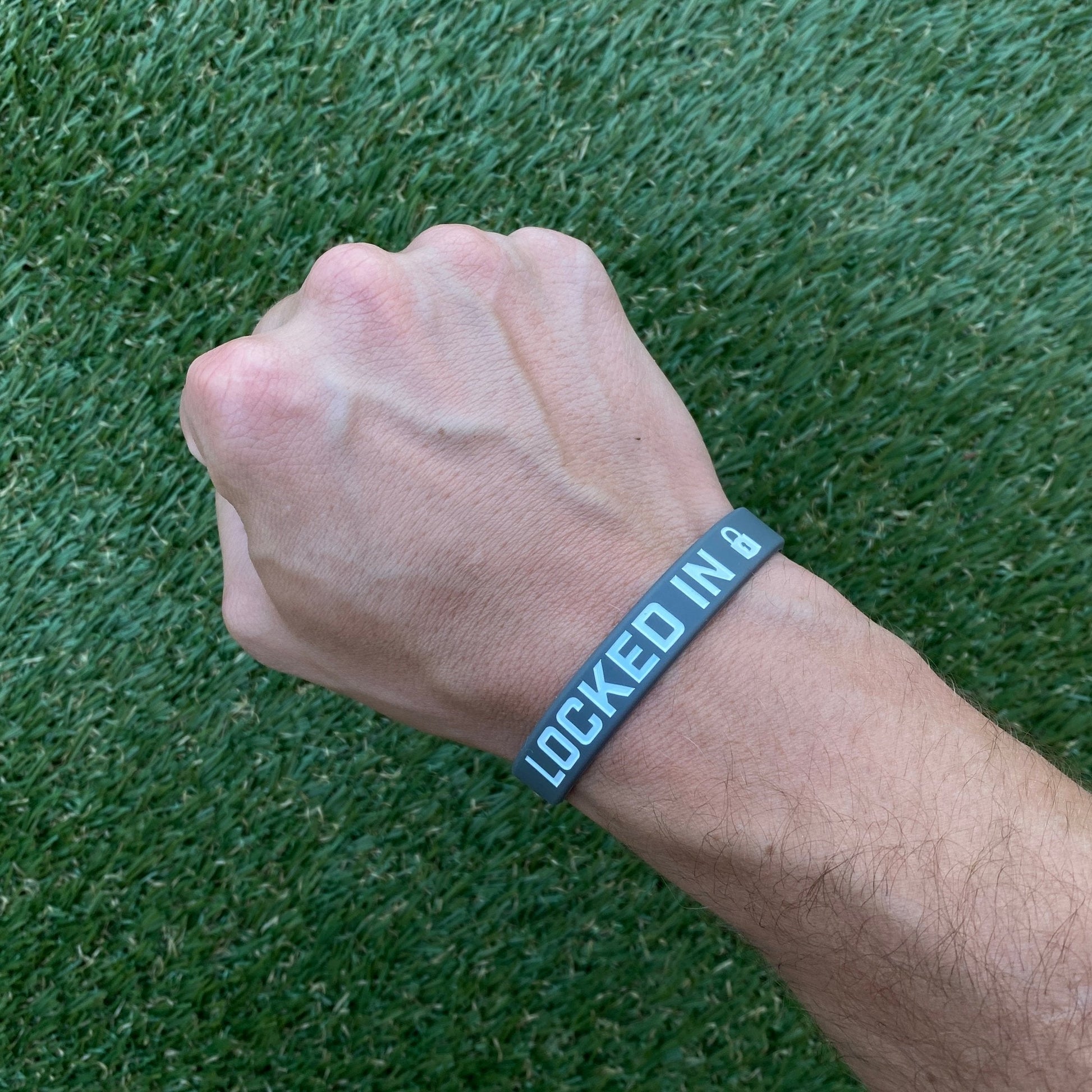 Hand wearing a wristband with 'LOCKED IN' text on a grass background