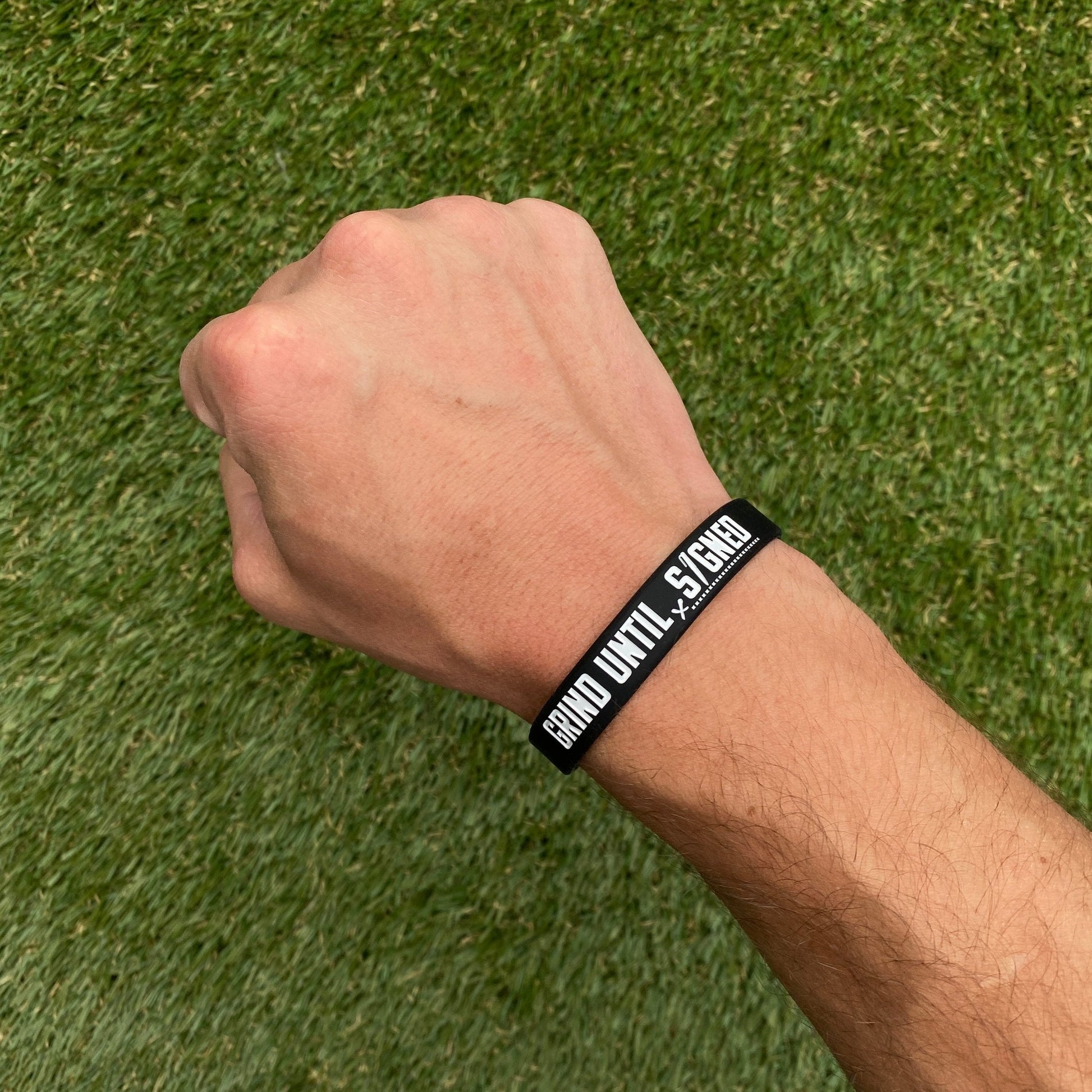 Hand wearing a black wristband with text on a grass background