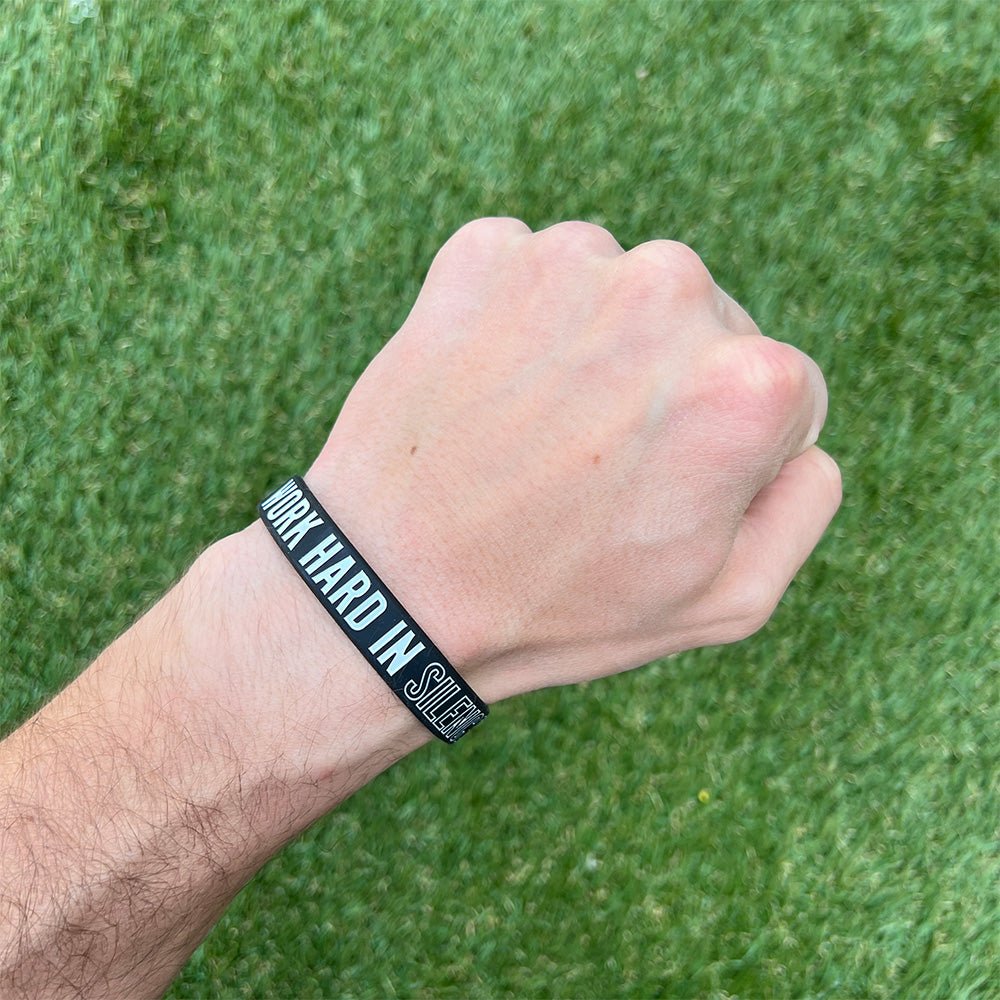 Hand wearing a black wristband with text on a grass background