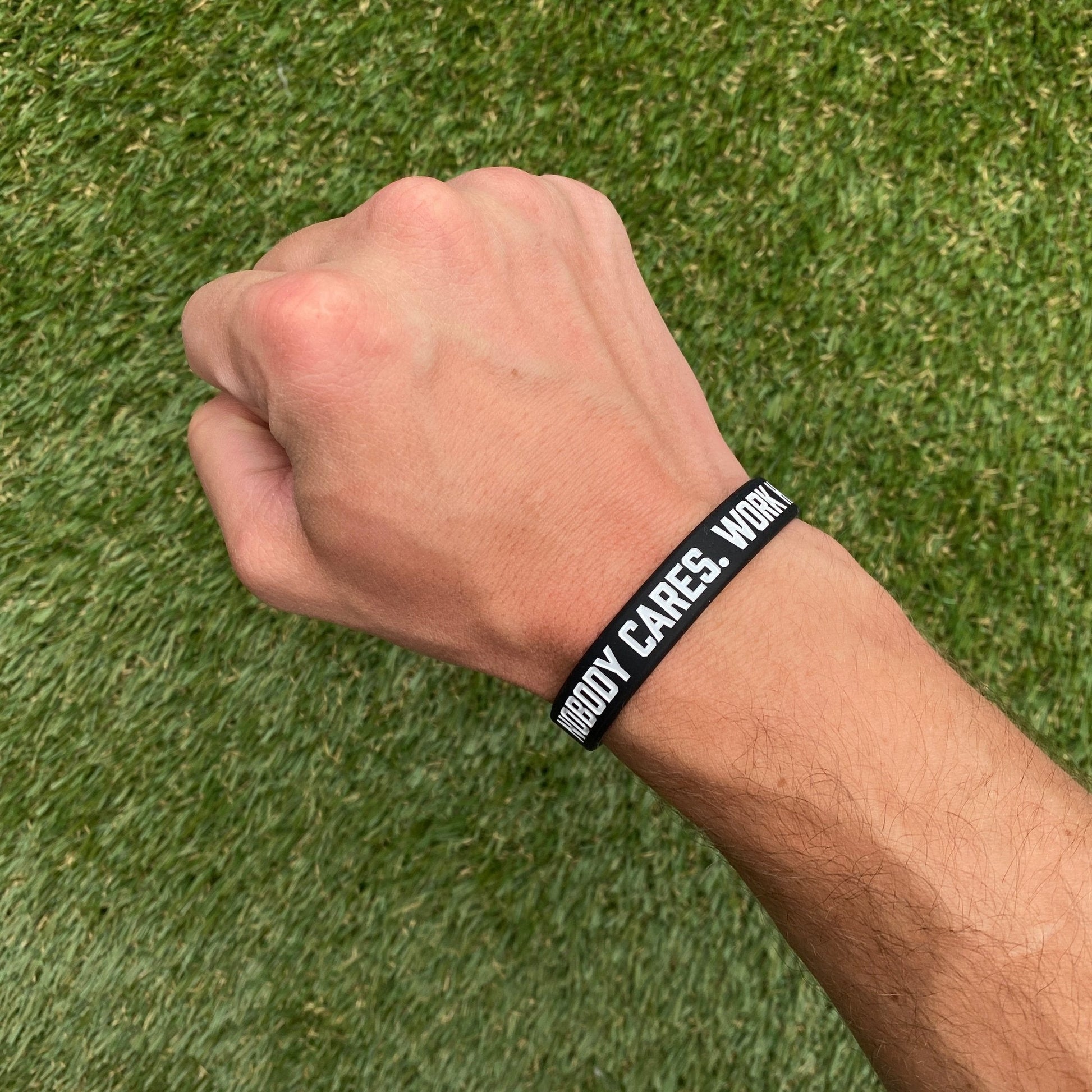 Hand wearing a black wristband with text on a grass background