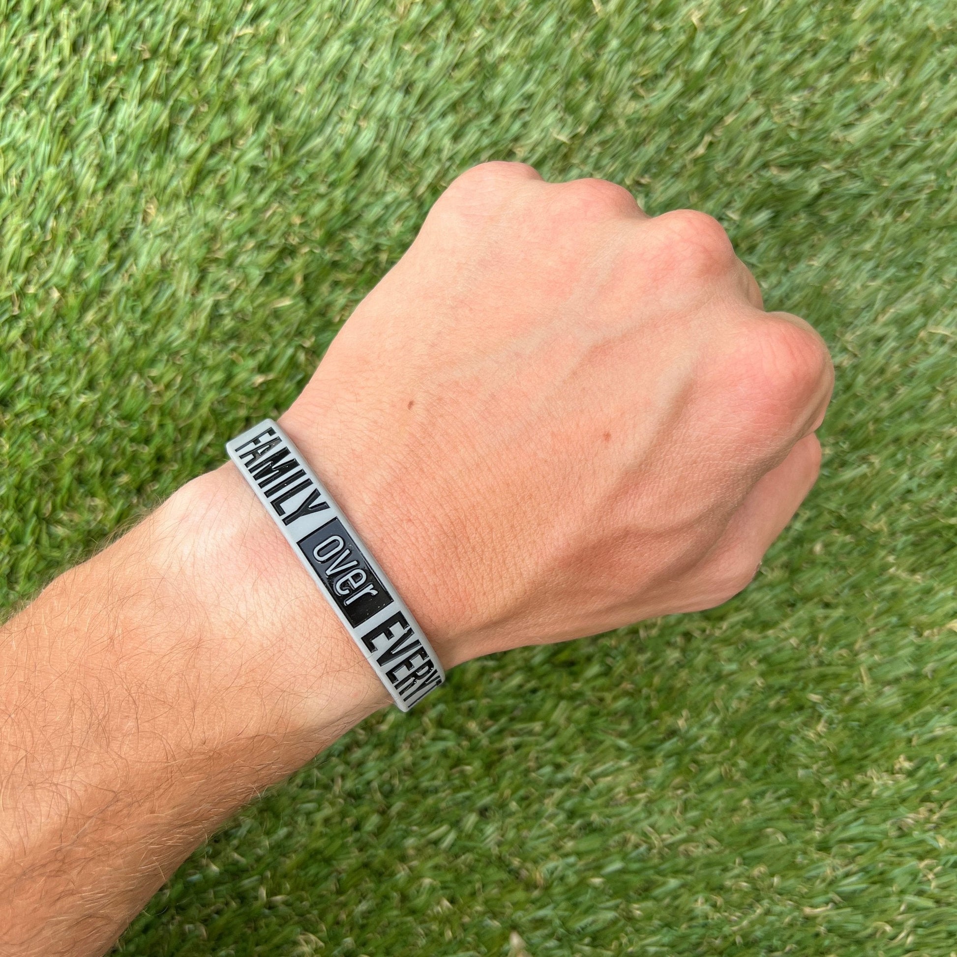 Hand wearing a bracelet with 'Family Over Everything' text on grass background