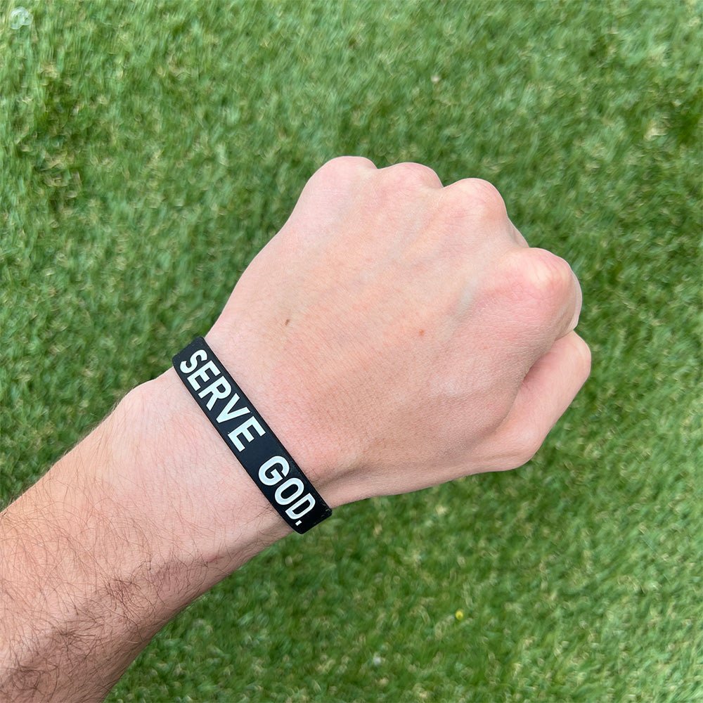 Hand wearing a black wristband with 'SERVE GOD' text against a green grass background