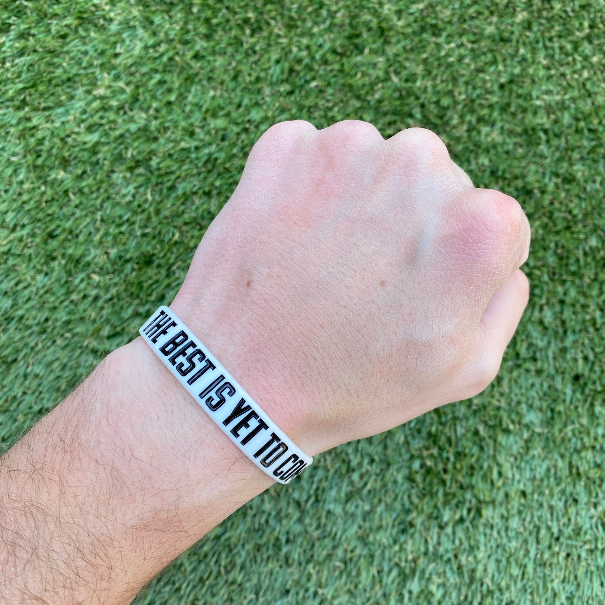 Hand wearing a wristband with 'The Best is Yet to Come' text on a grass background