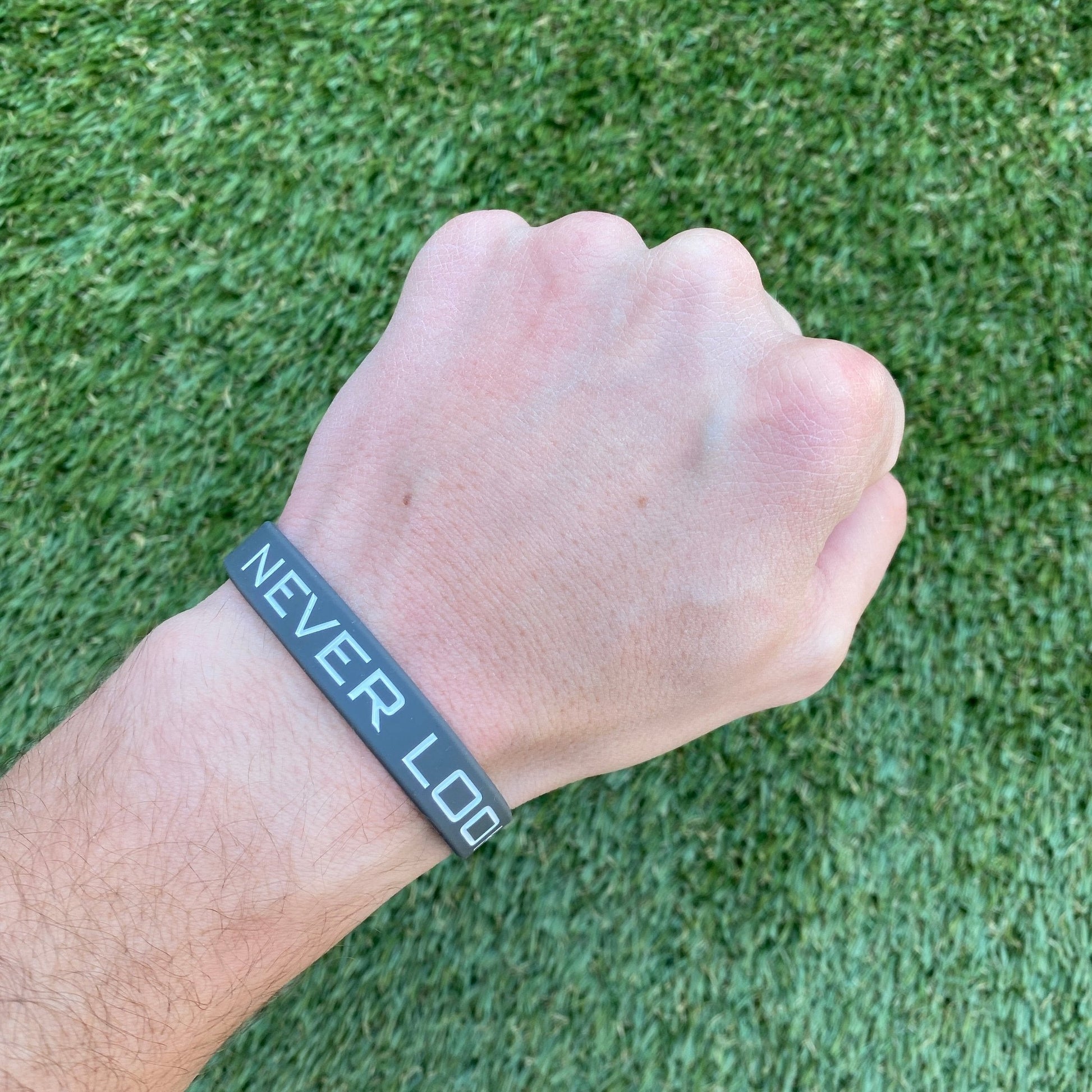 Hand wearing a wristband with 'NEVER LOSE' text on a grass background