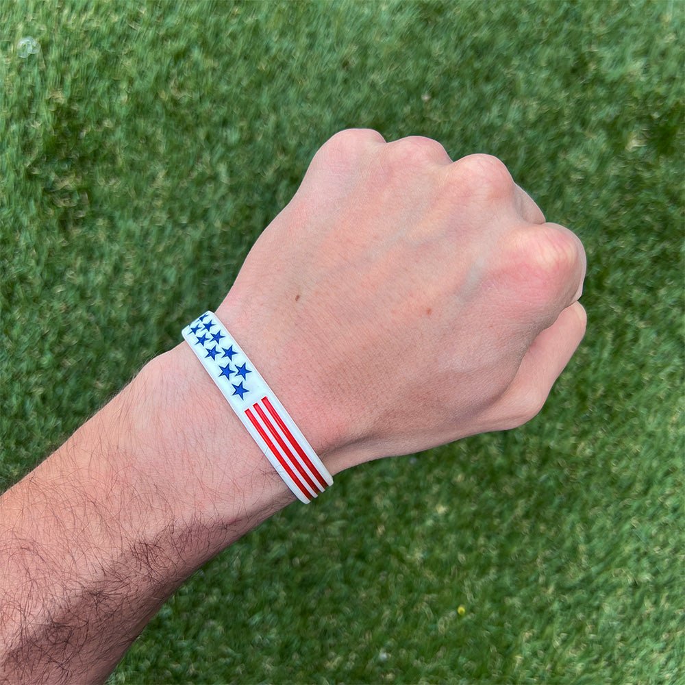 Hand wearing a wristband with an American flag design on a grass background
