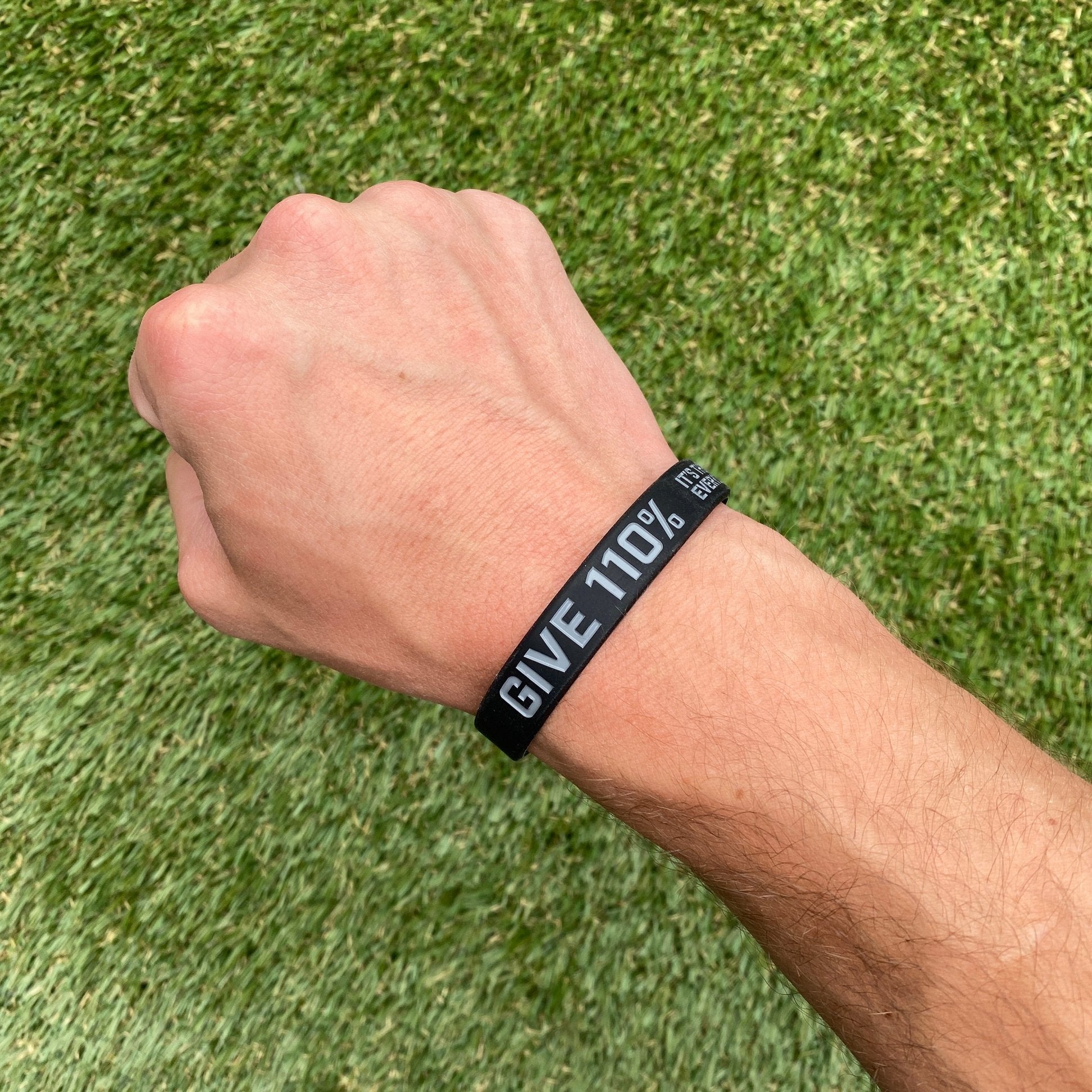 Wrist wearing a black 'GIVE 110%' wristband on a grass background