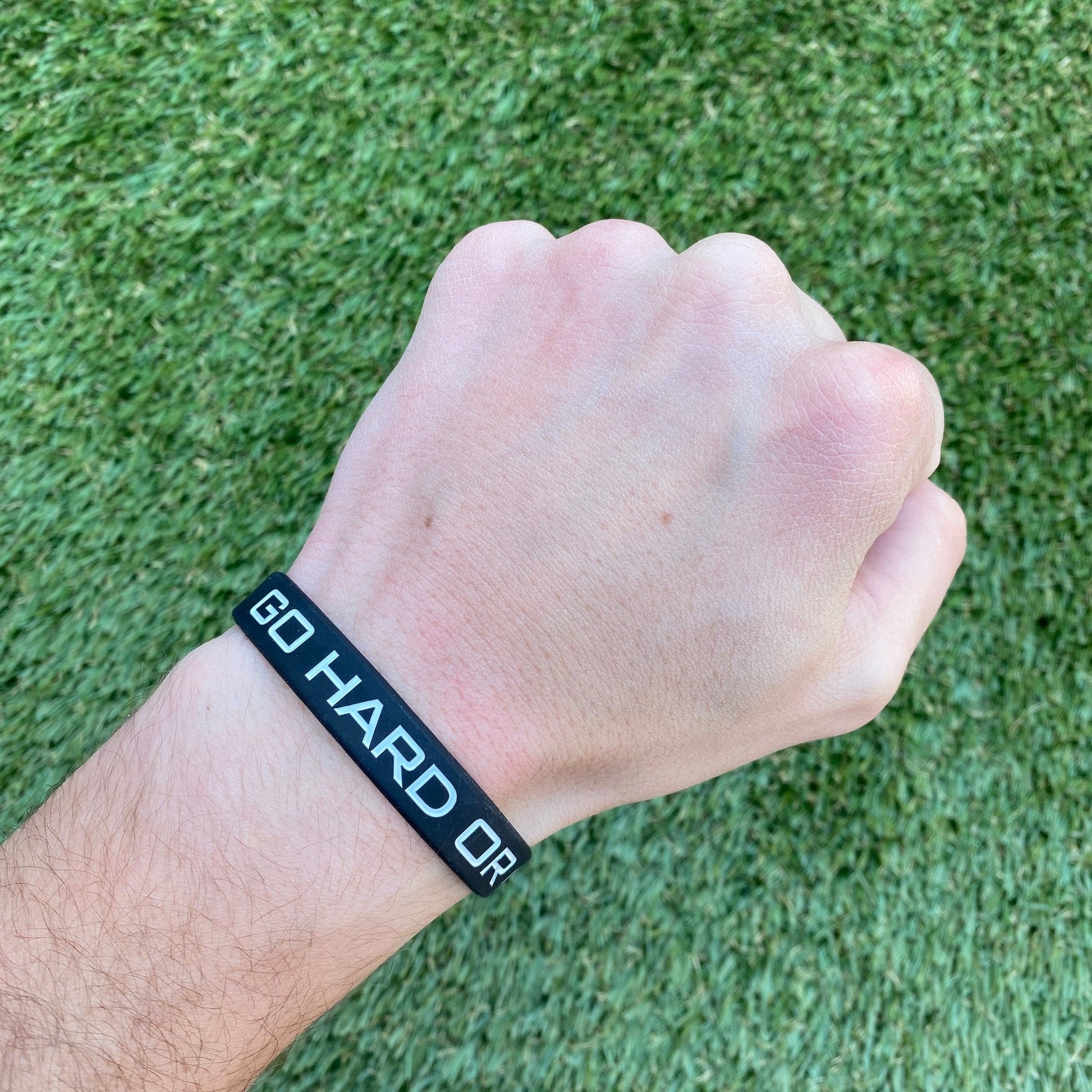 Hand wearing a black wristband with 'GO HARD OR' text on green grass background
