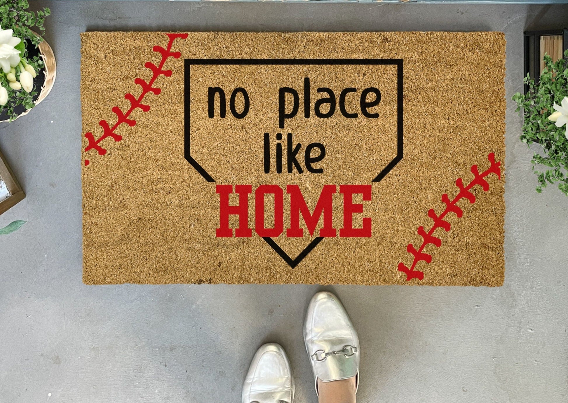 Doormat with 'no place like HOME' text and baseball design on a concrete floor.