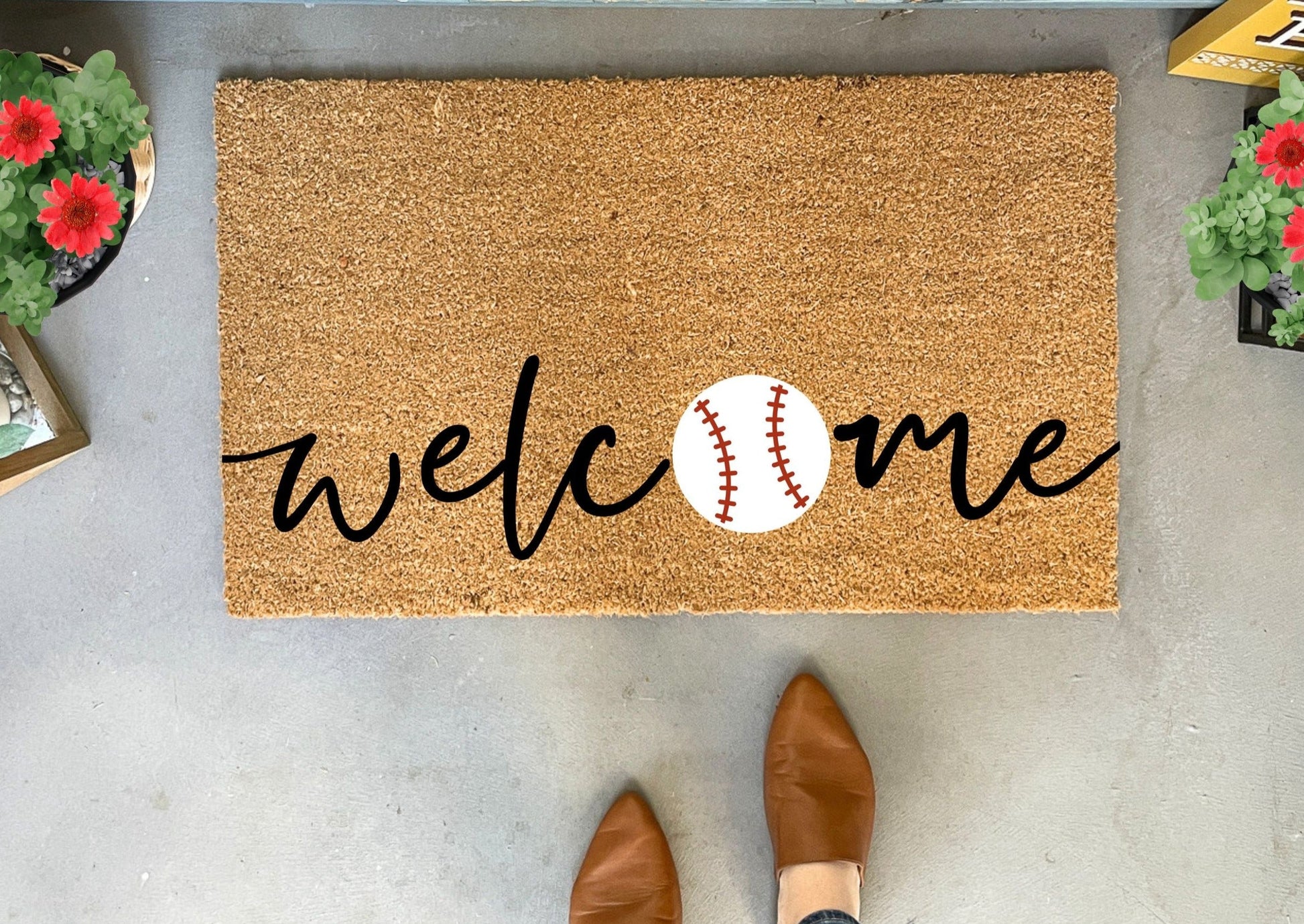 Doormat with 'welcome' and baseball design on a concrete floor.