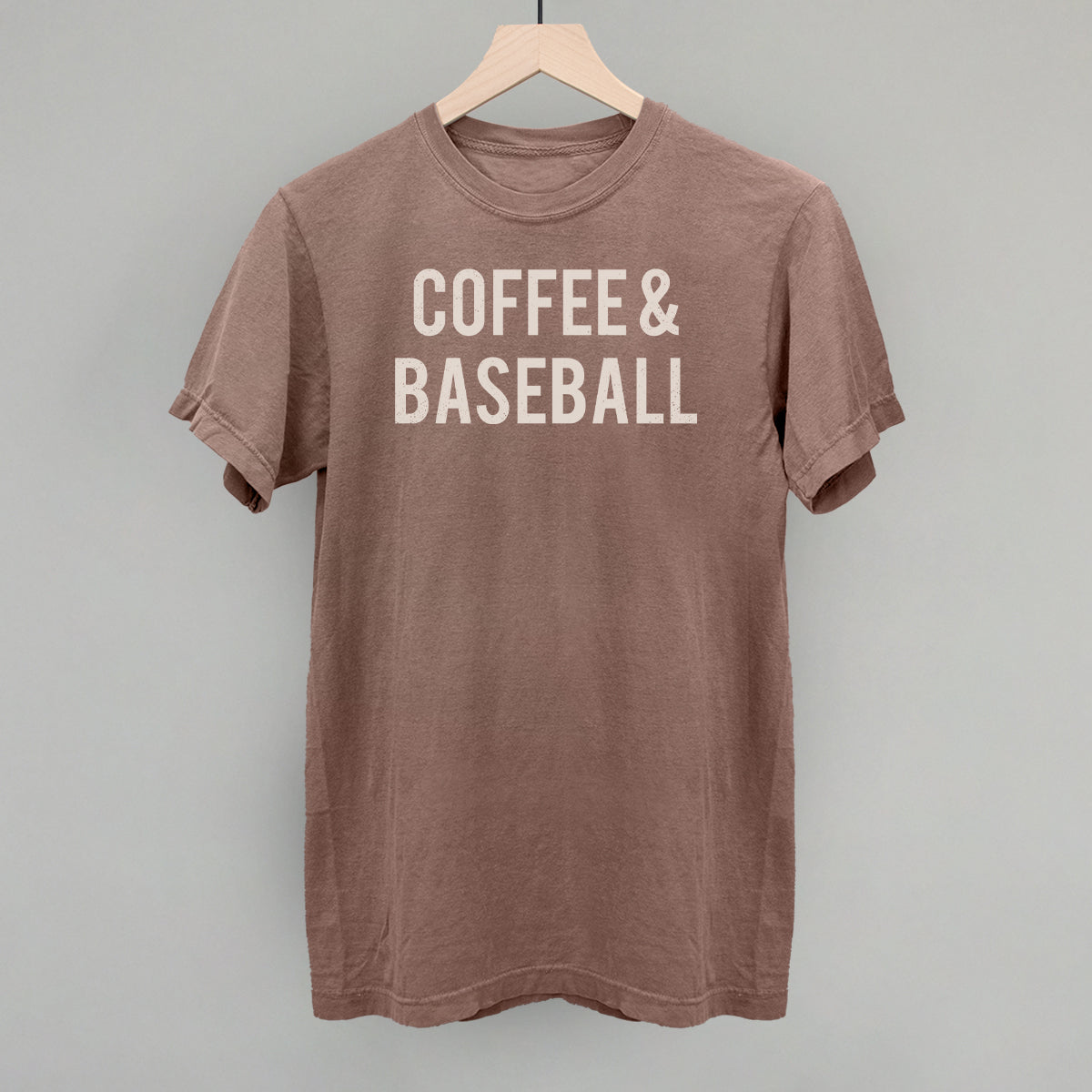 Brown comfort colors t-shirt with 'COFFEE & BASEBALL' text on a hanger against a gray background