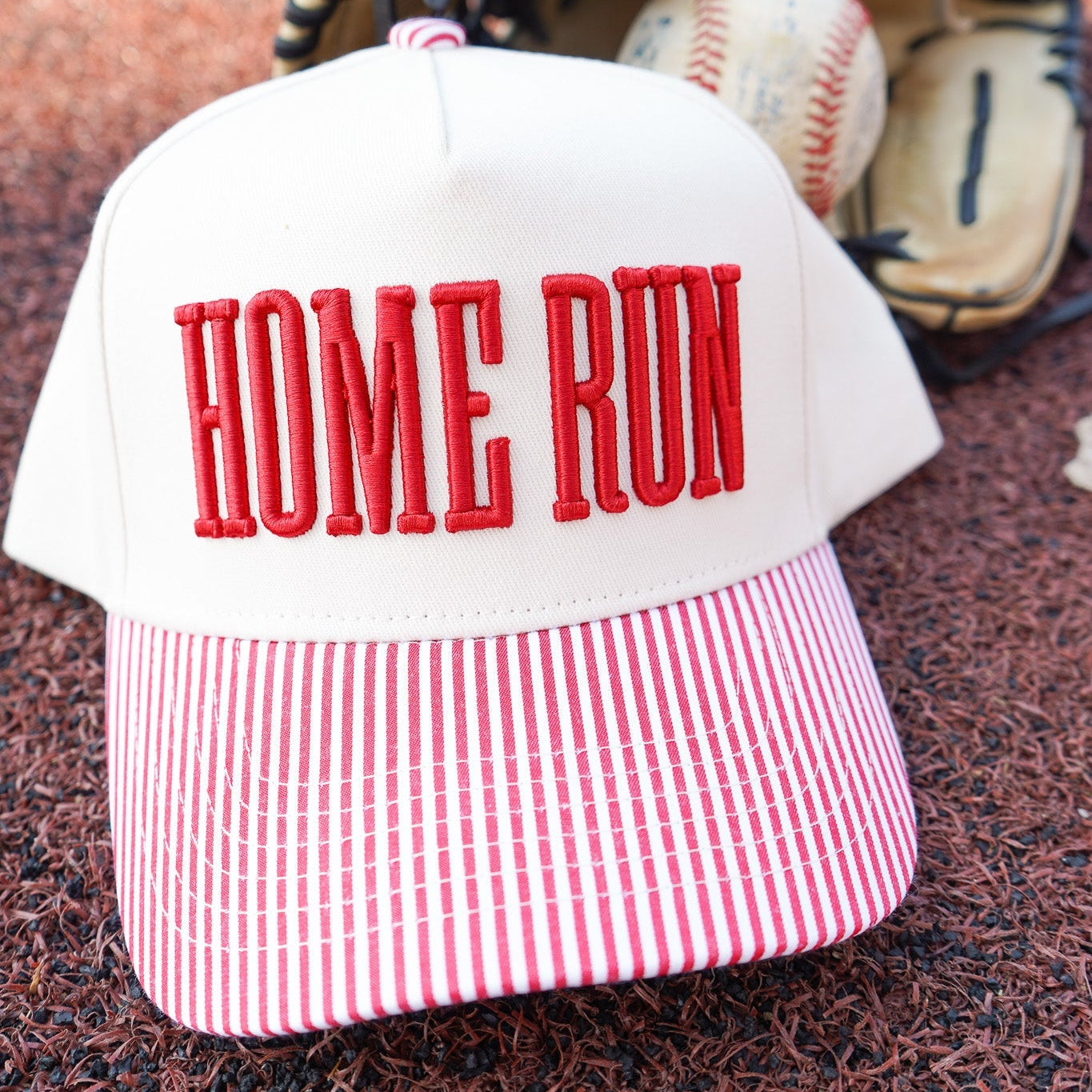 Baseball cap with 'HOME RUN' text on a baseball field, next to a baseball and glove.