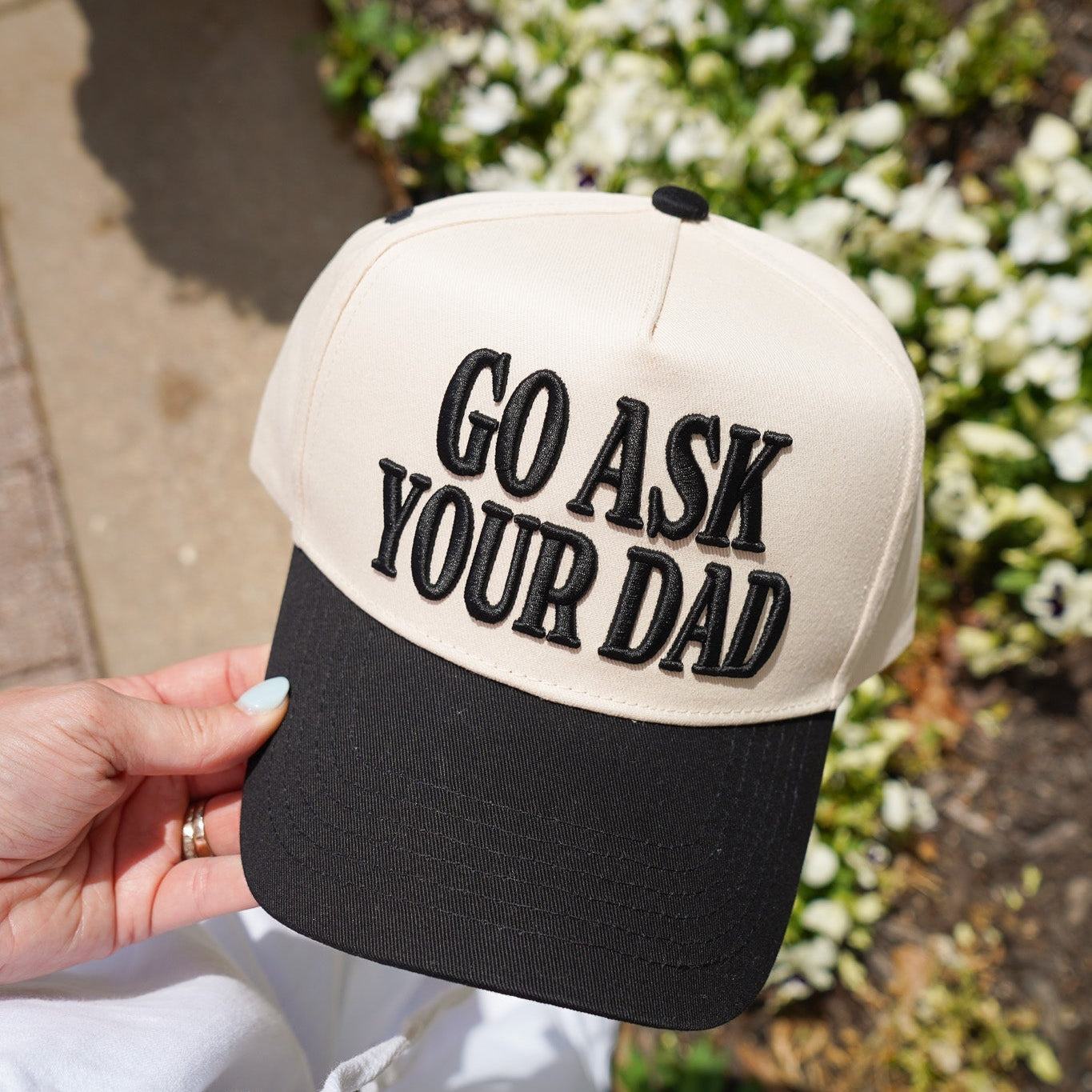 Cap with 'Go Ask Your Dad' text held by a person outdoors.