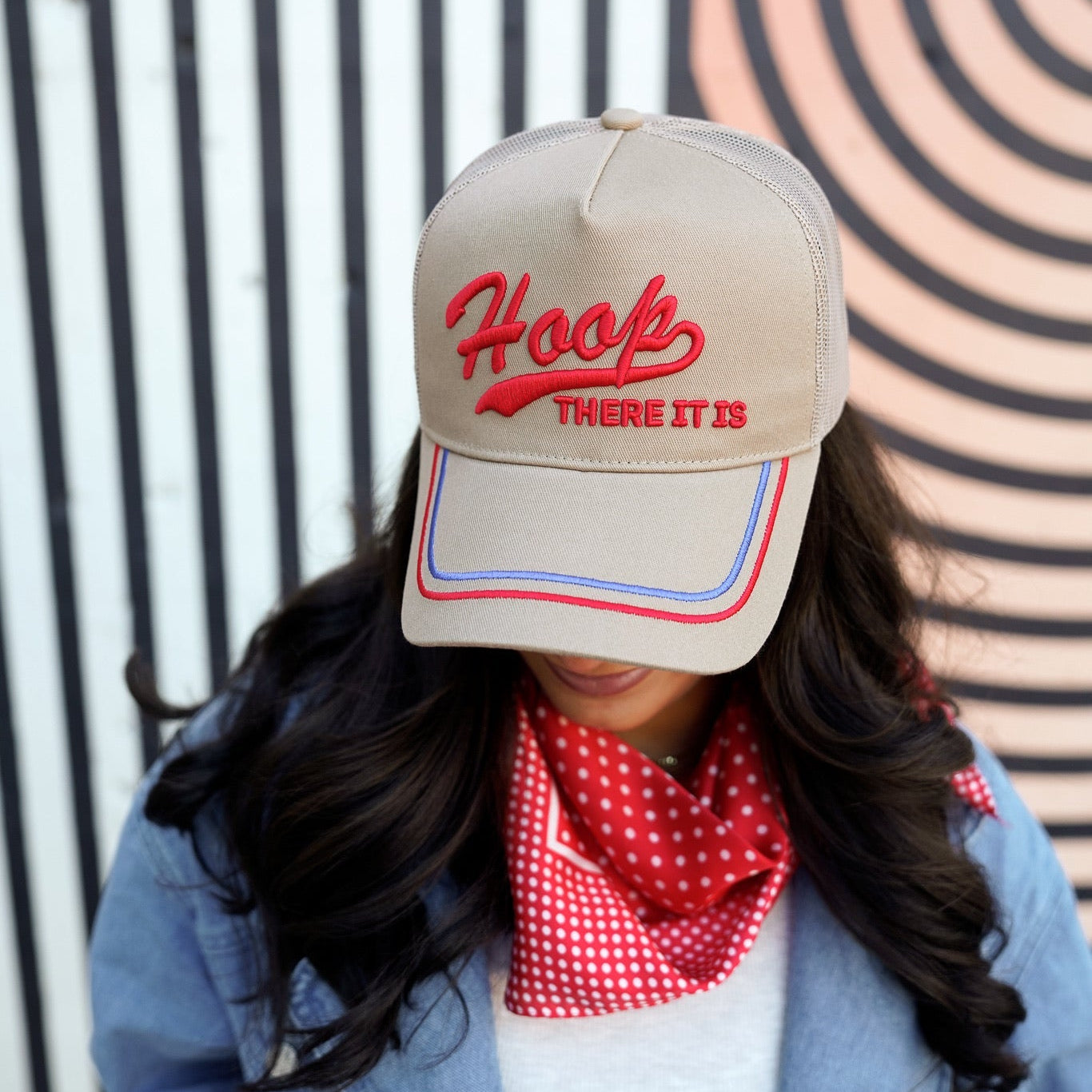 Collection of Person wearing a beige cap with red text and a red checkered scarf, standing against a striped background. in a gallery layout