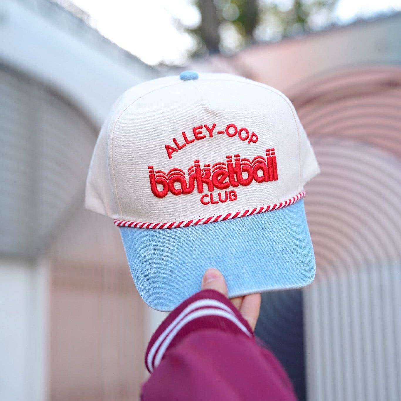 Collection of Cap with 'Alley-Oop Basketball Club' text held by a person wearing a maroon jacket. in a gallery layout