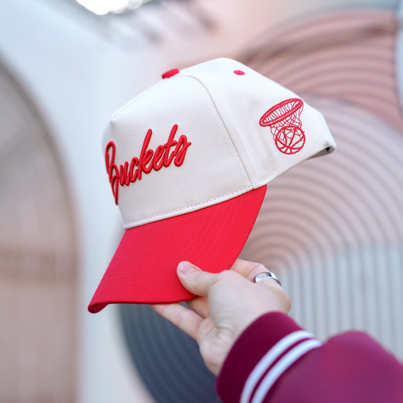 Red and white cap with 'Buckeyes' text held by a person wearing a maroon jacket.
