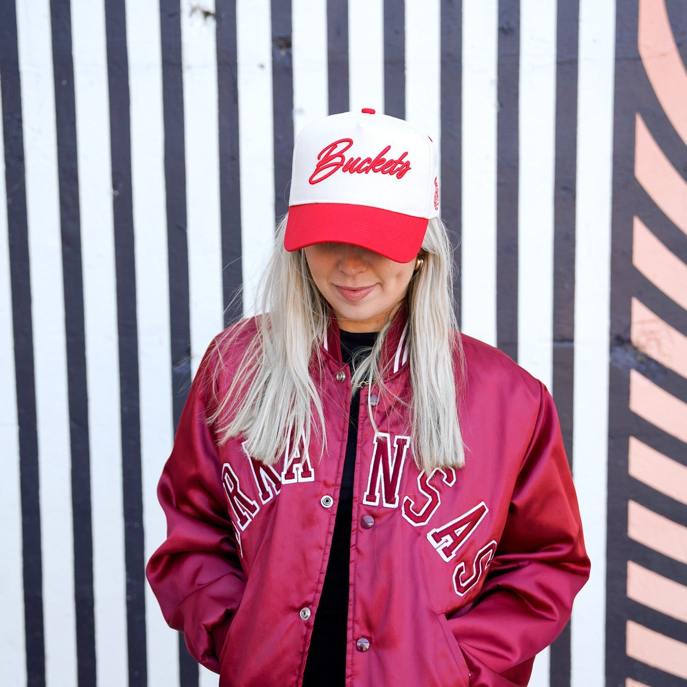 Collection of Person wearing a red varsity jacket and white cap with red text against a striped background in a gallery layout
