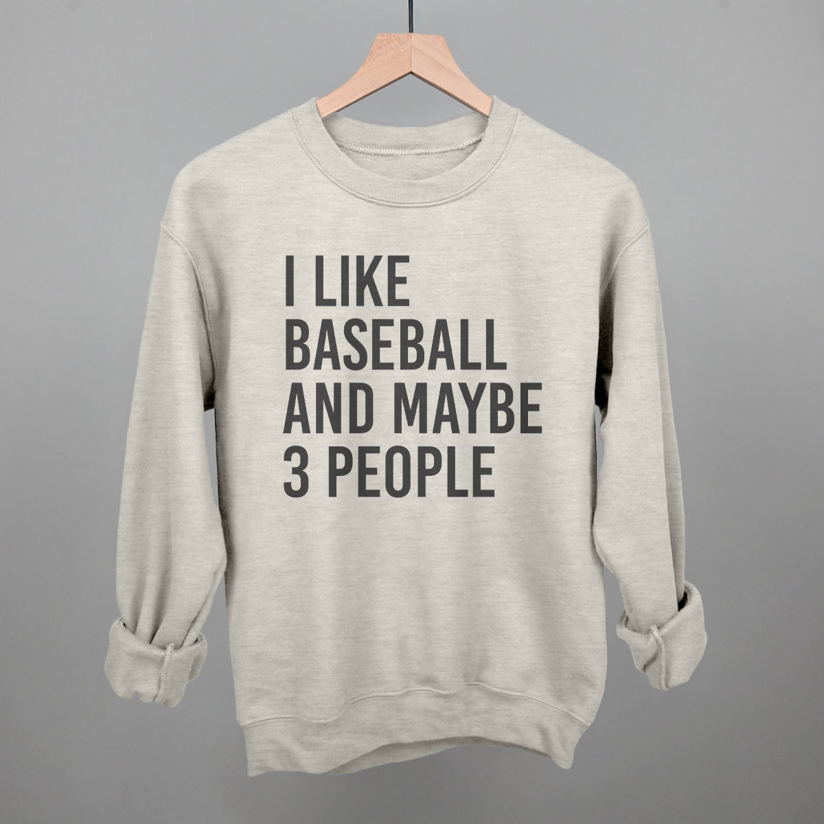 oatmeal color sweatshirt with 'I like baseball and maybe 3 people' text on a hanger against a gray background