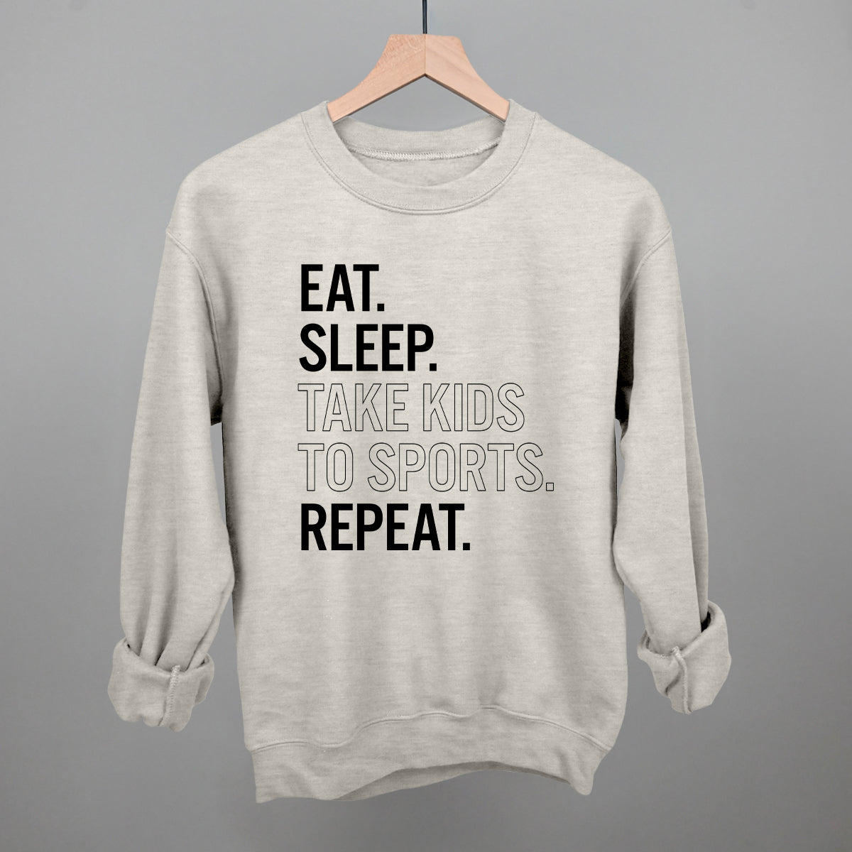 Collection of oatmeal comfort colors sweatshirt with text 'EAT. SLEEP. TAKE KIDS TO SPORTS. REPEAT.' on a gray background in a gallery layout