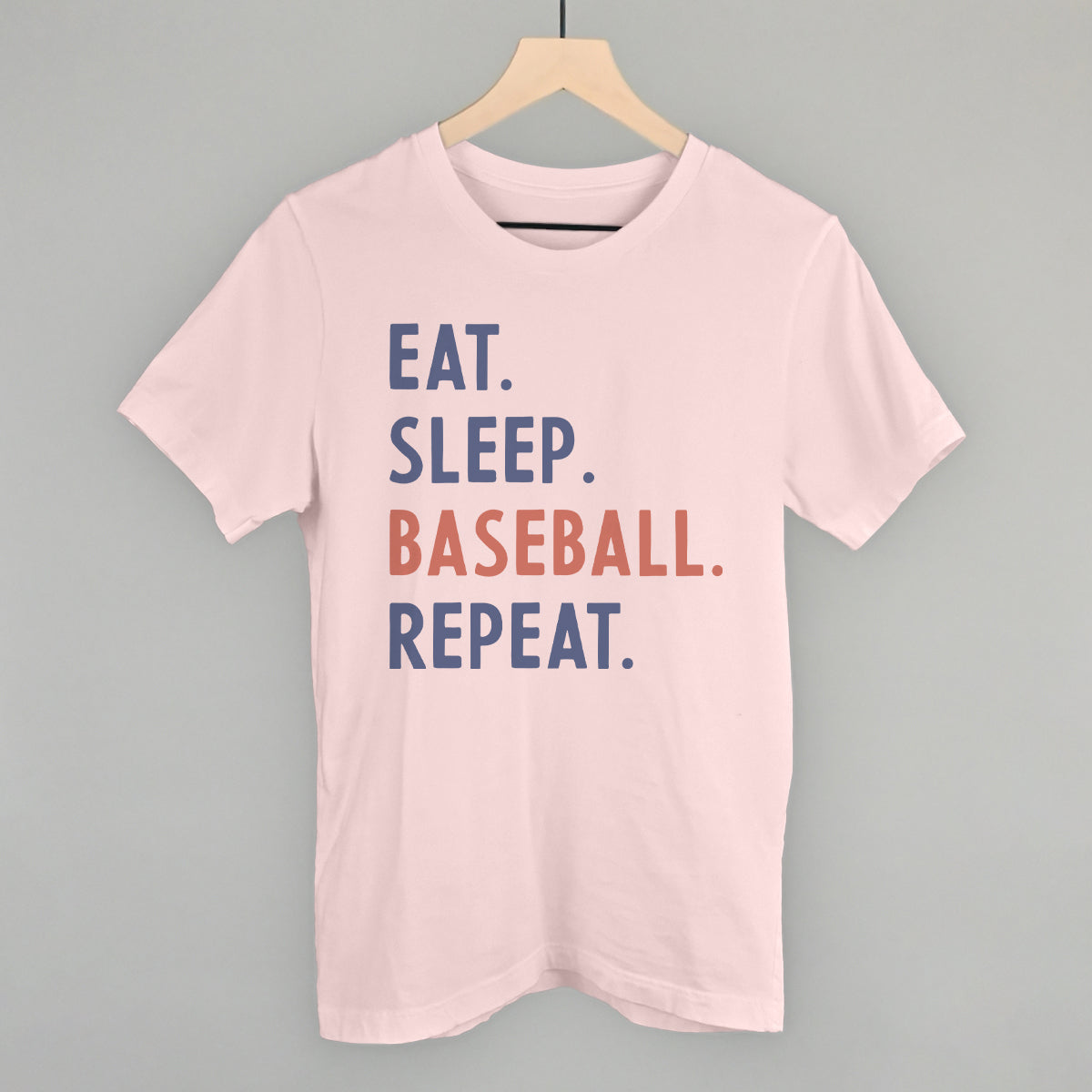 Pink t-shirt with 'Eat. Sleep. Baseball. Repeat.' text on a hanger against a gray background