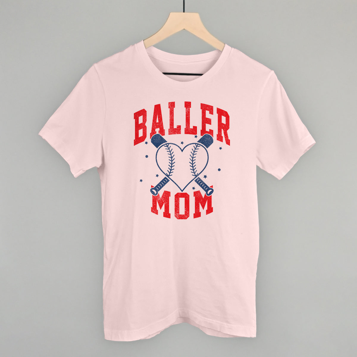 Pink t-shirt with 'Baller Mom' text on a hanger against a gray background