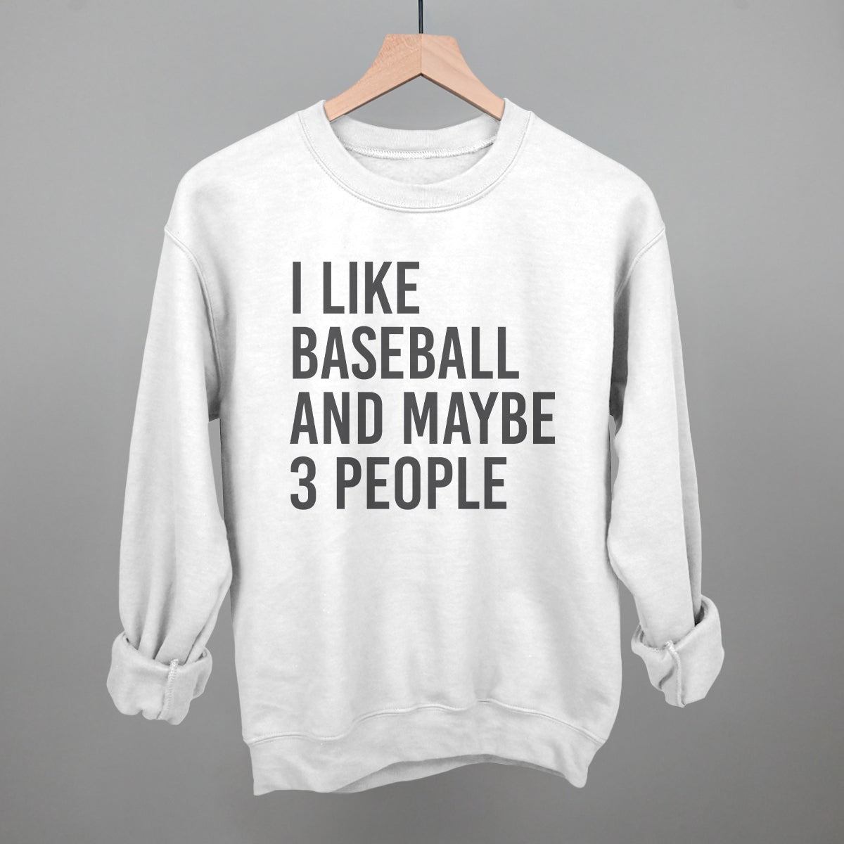White sweatshirt with text 'I LIKE BASEBALL AND MAYBE 3 PEOPLE' on a hanger against a gray background