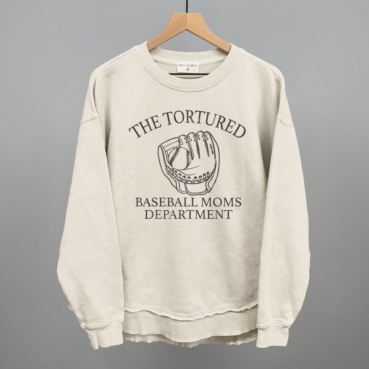 Beige sweatshirt with 'The Tortured Baseball Moms Department' text and graphic on a hanger against a gray background