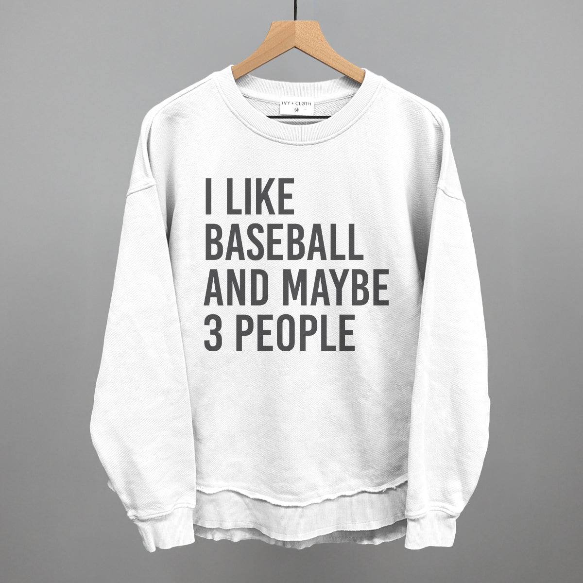 Collection of White sweatshirt with text 'I LIKE BASEBALL AND MAYBE 3 PEOPLE' on a hanger against a gray background in a gallery layout