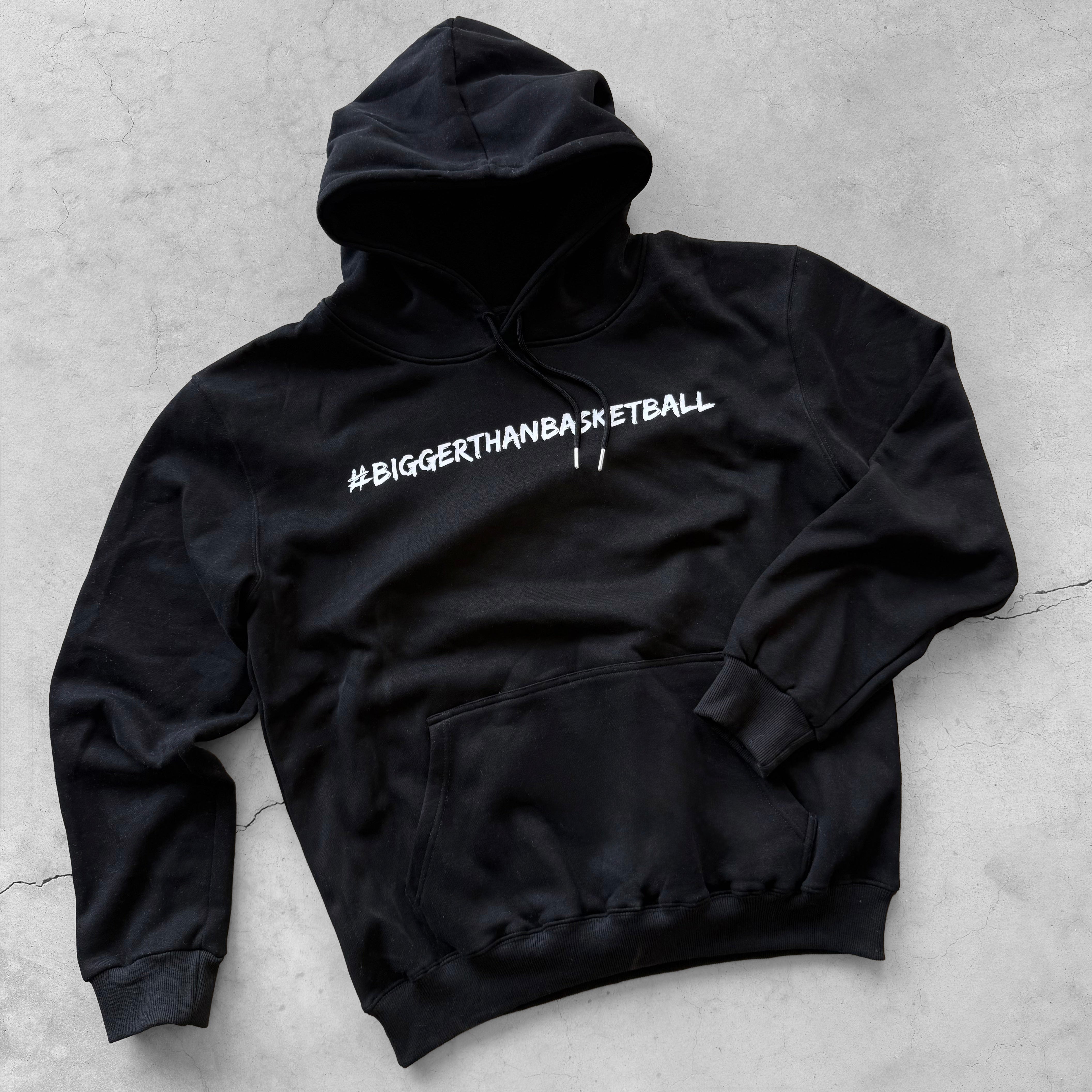 Collection of Black hoodie with '#BIGGERTHANBASKETBALL' text on a gray surface in a gallery layout