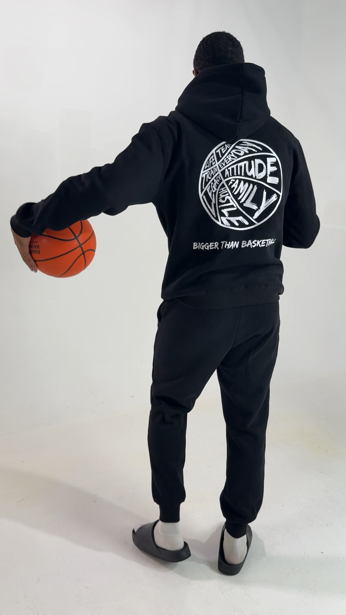 Collection of Person wearing a black hoodie with a logo and text, holding a basketball on a white background in a gallery layout