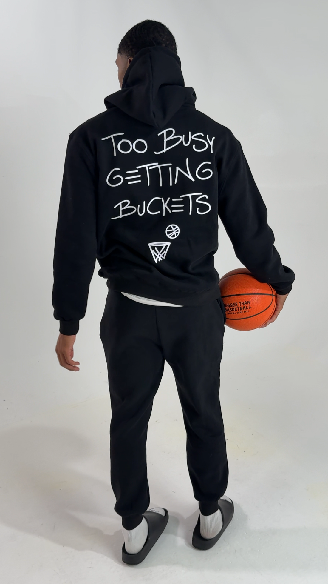 Person wearing a black hoodie with text and holding a basketball on a white background