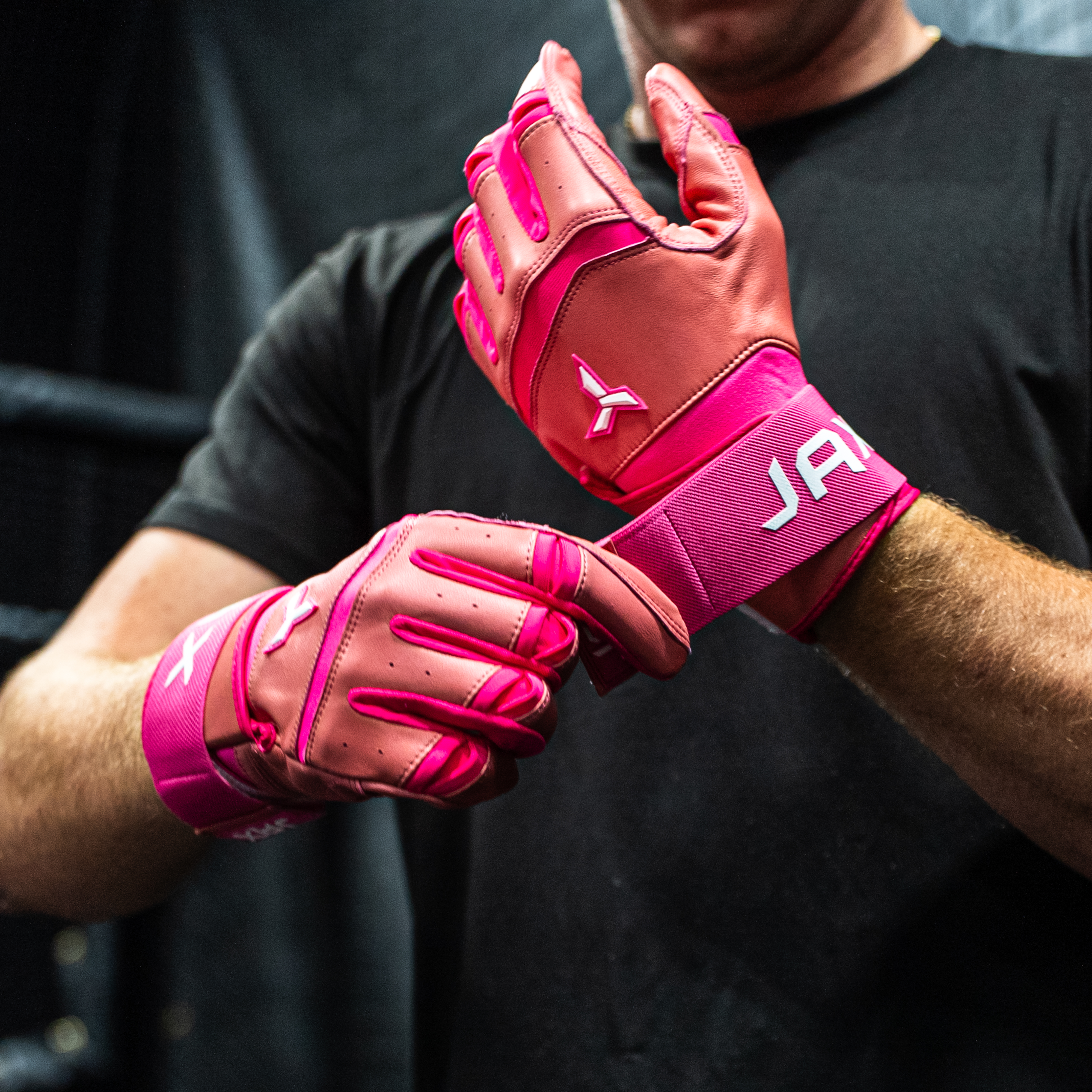 Collection of Person wearing pink JAX batting gloves with a brand logo on a black background in a gallery layout
