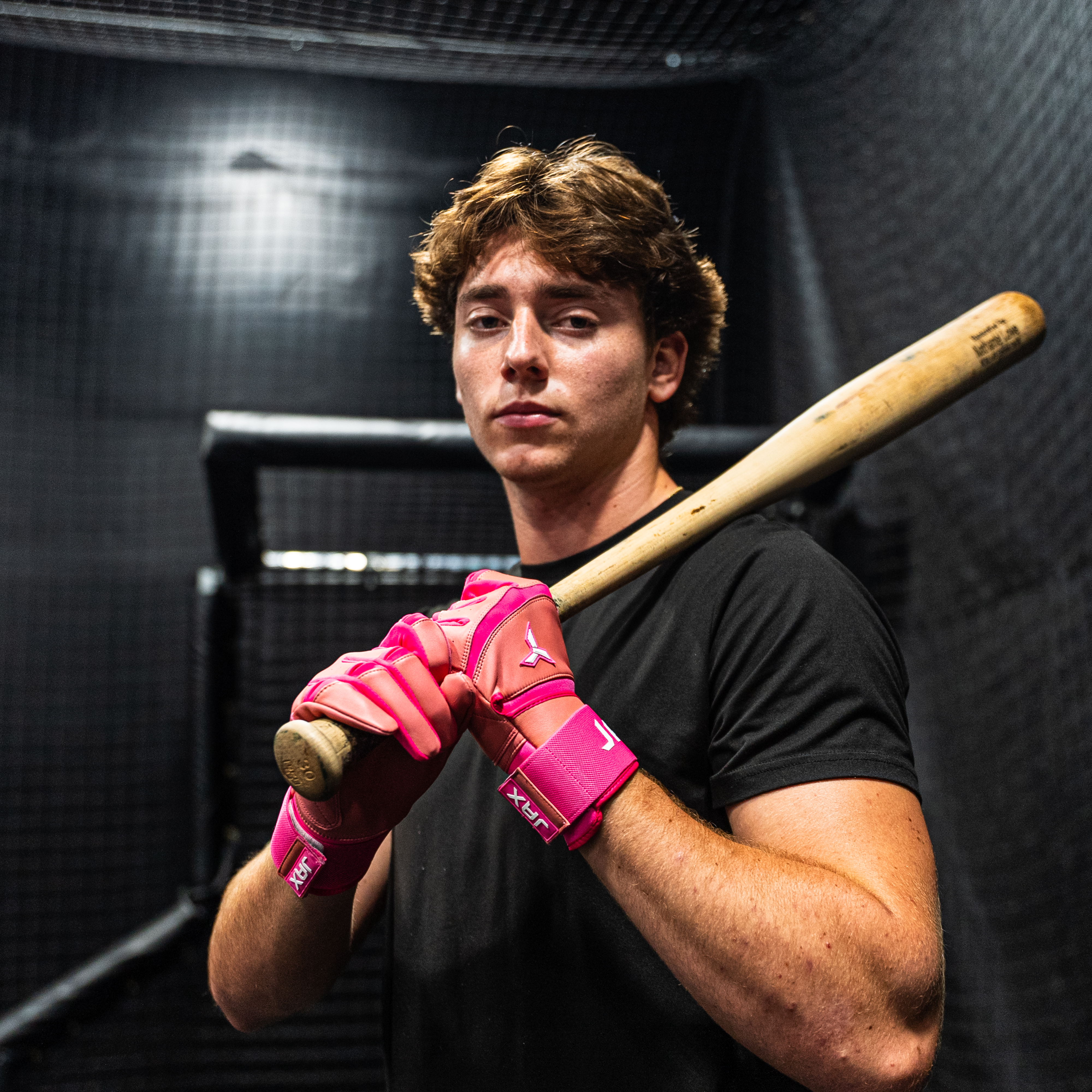 Collection of Person holding a baseball bat with pink batting gloves in a dark indoor setting in a gallery layout