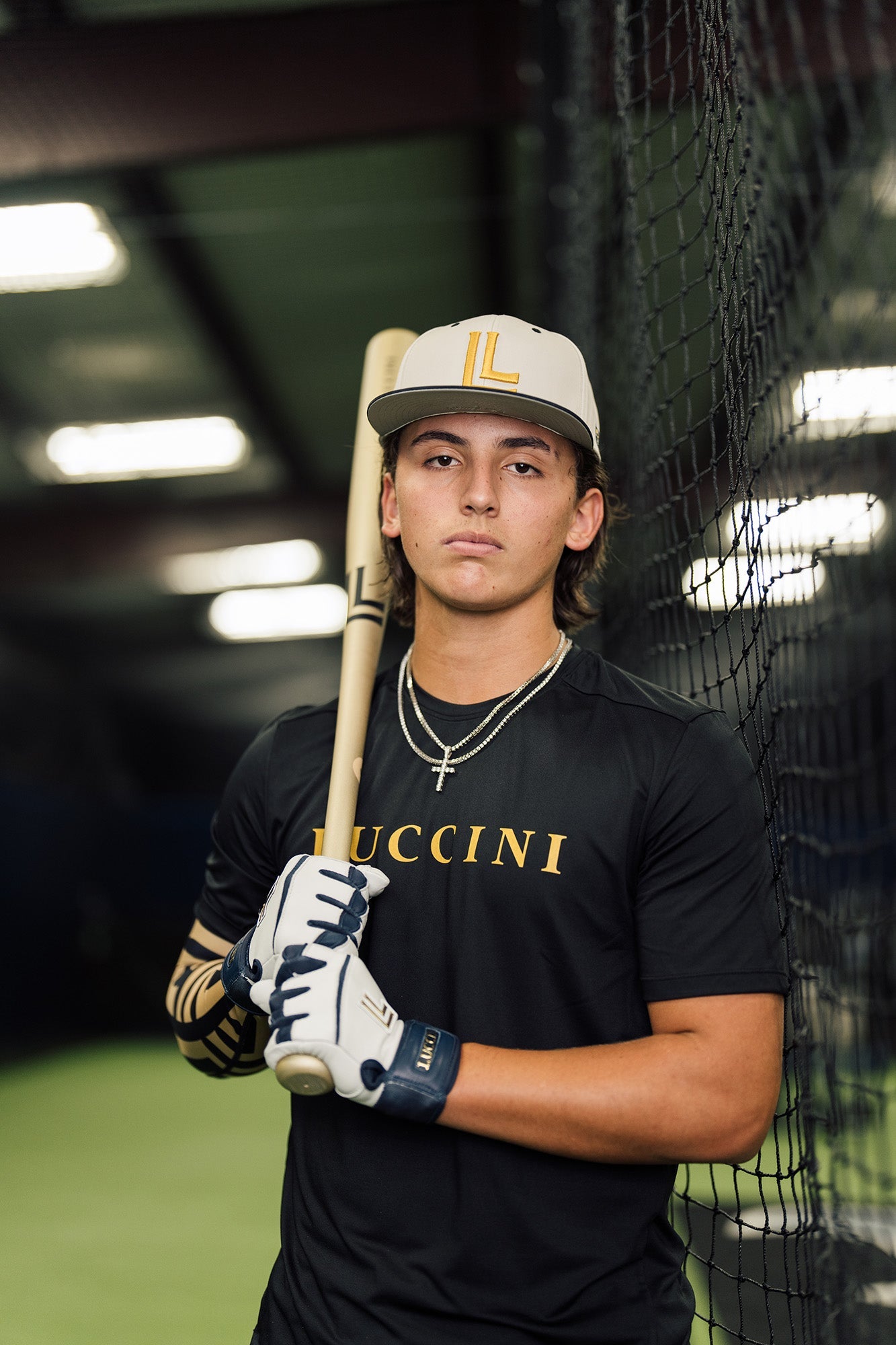 Collection of Person holding a baseball bat in front of a batting cage, wearing a black shirt with 'Lucchini' branding. in a gallery layout