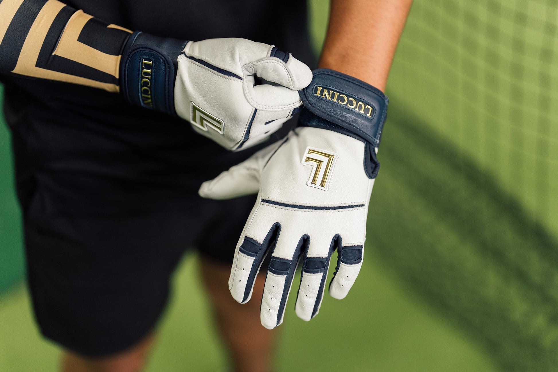 Person wearing Lucchini branded batting gloves on a blurred green background