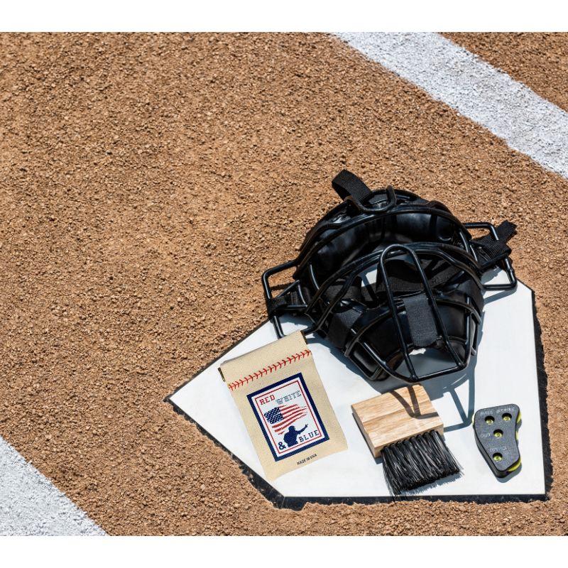 Collection of Baseball mask, cleaning brush, and cloth on a dirt surface with a white line. in a gallery layout