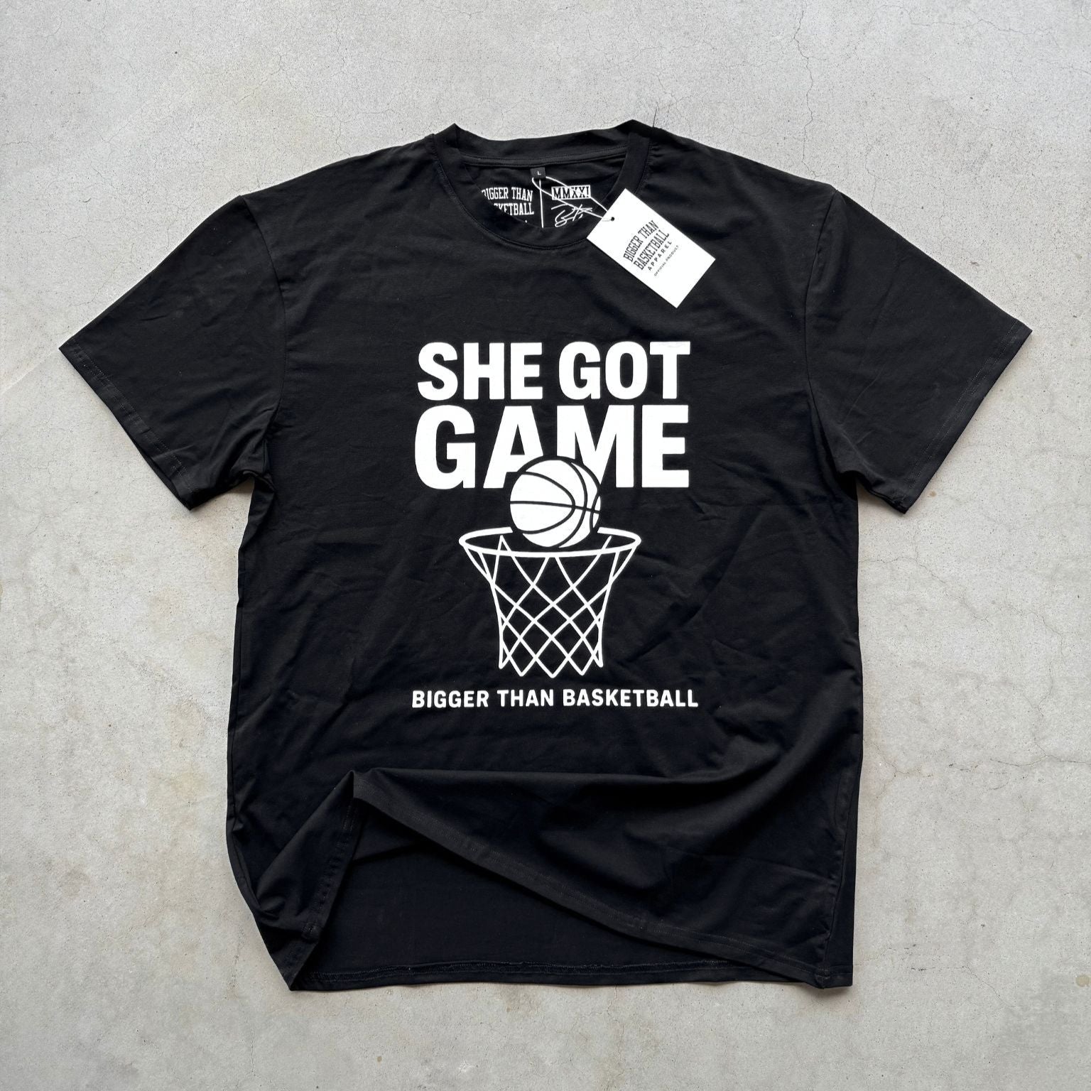 Collection of Black t-shirt with 'She Got Game Bigger Than Basketball' text and graphics on a gray surface in a gallery layout