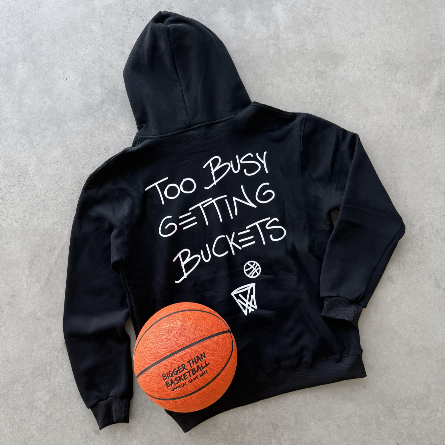 Collection of Black hoodie with 'Too Busy Getting Buckets' text and a basketball on a gray surface in a gallery layout