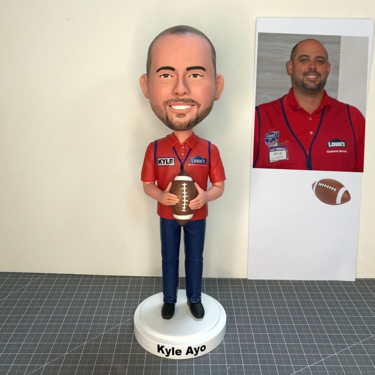 Bobblehead of a man in a red shirt holding a football, with a photo of the same person in the background.