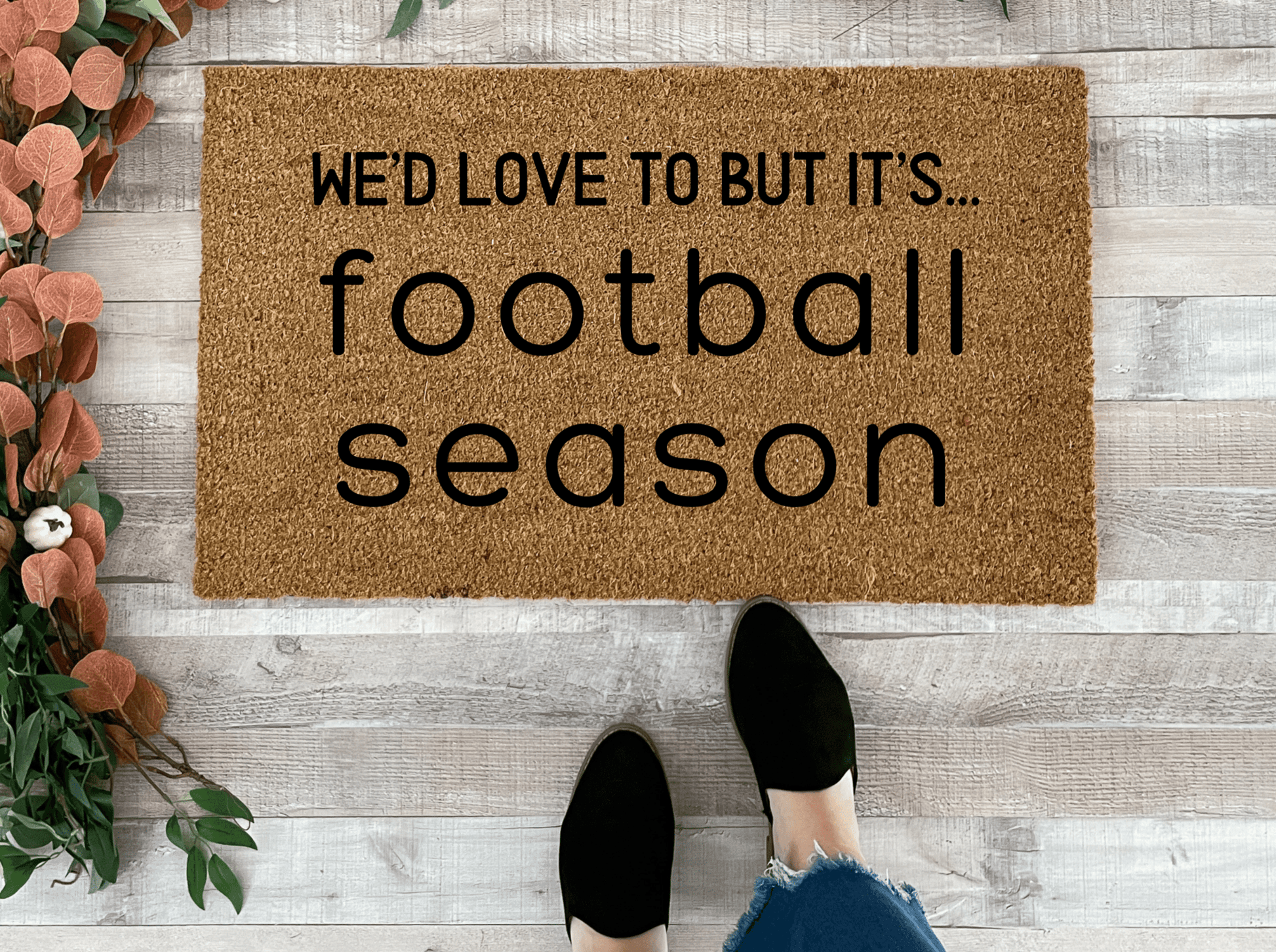 Doormat with 'We'd love to but it's football season' text on a wooden floor.