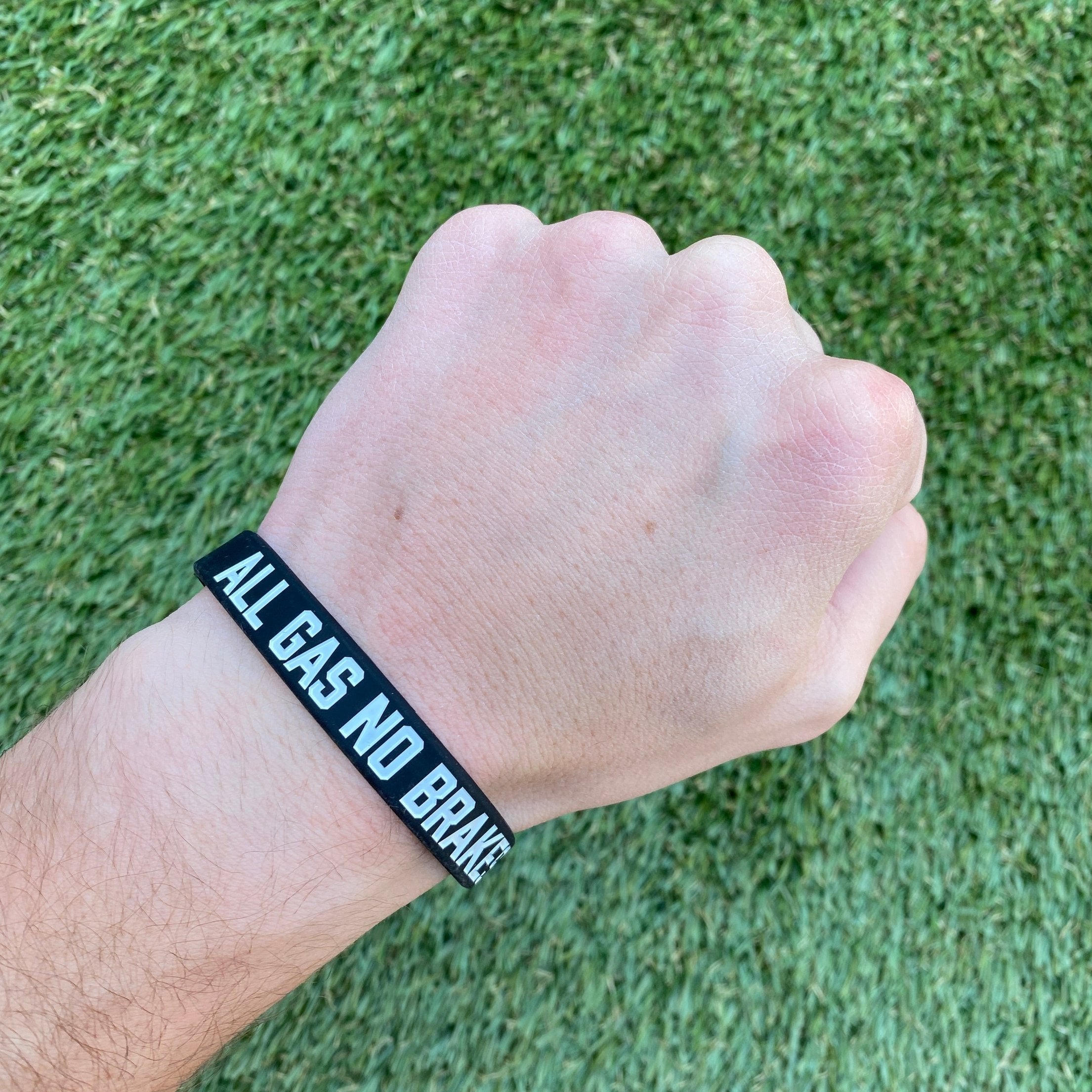 Collection of Hand wearing a black wristband with 'ALL GAS NO BRAKE' text on a grass background in a gallery layout