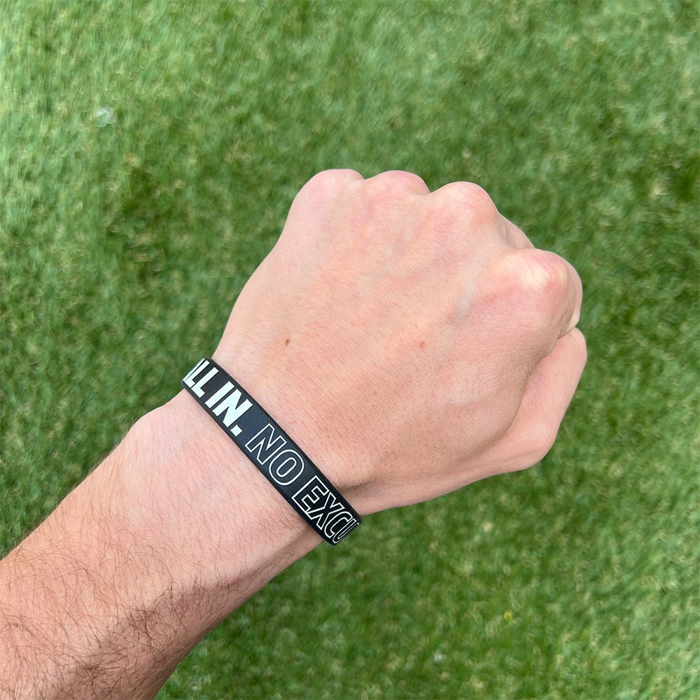 Hand wearing a black wristband with white text against a green grass background