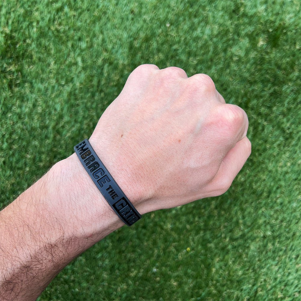 Hand wearing a black wristband with text on a green grass background