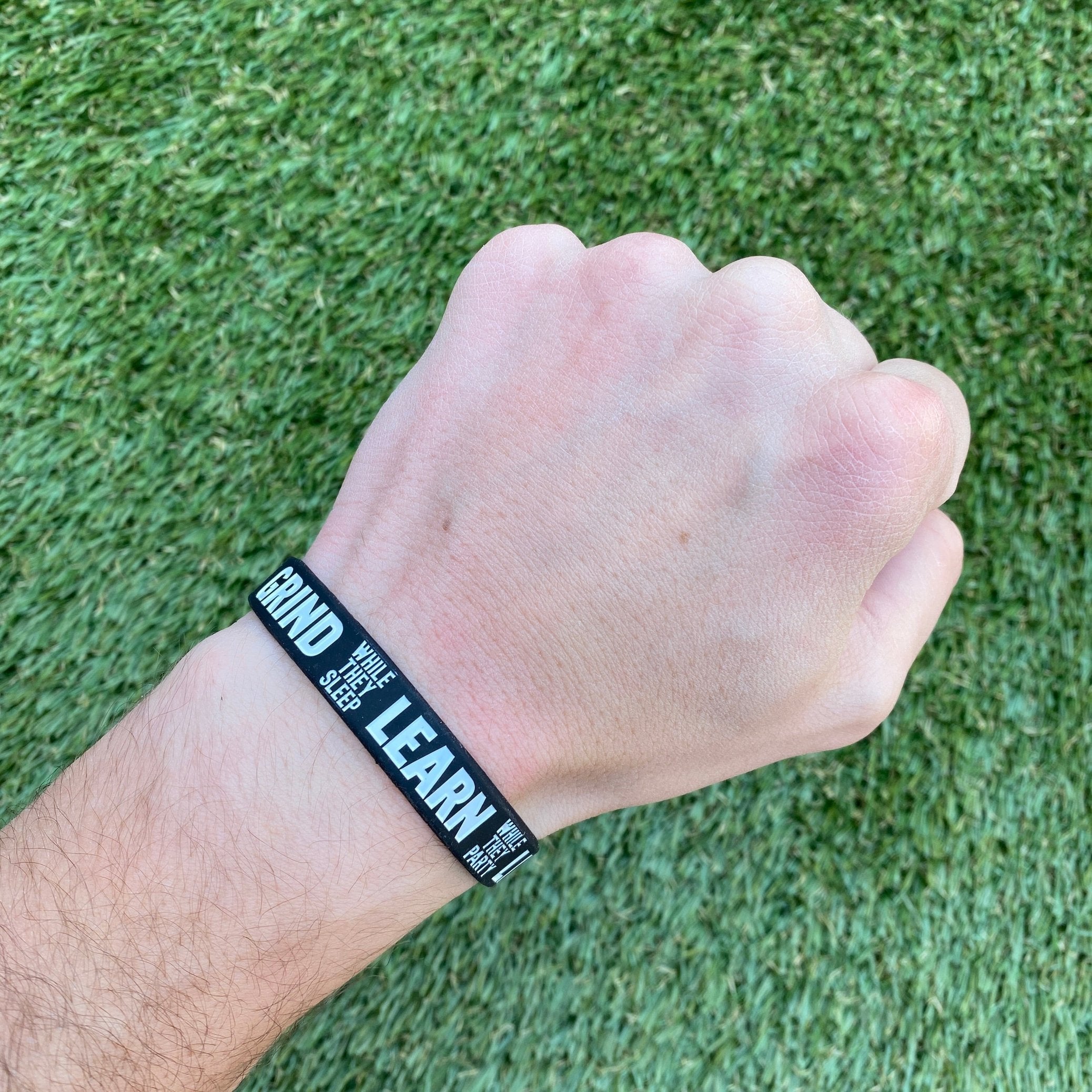 Collection of Hand wearing a black wristband with text on a grass background in a gallery layout