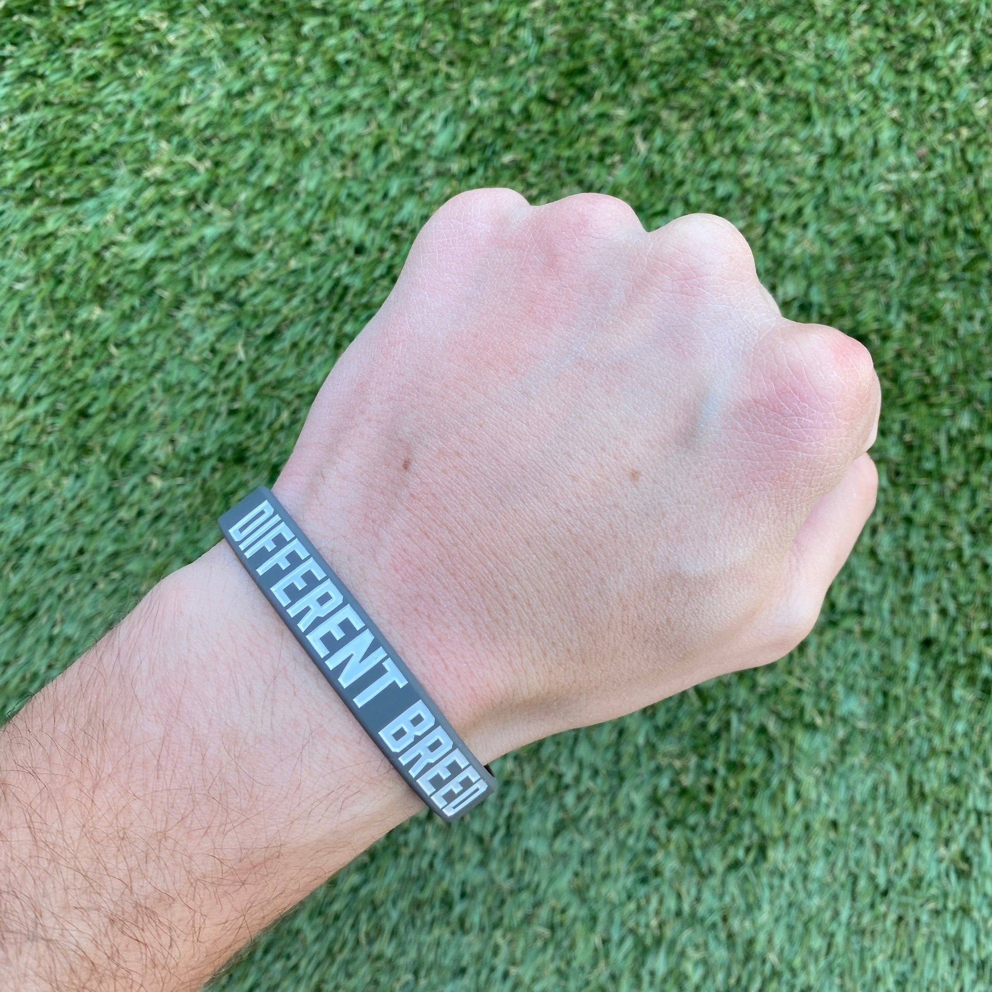 Hand wearing a wristband with 'Different Breed' text on a grass background