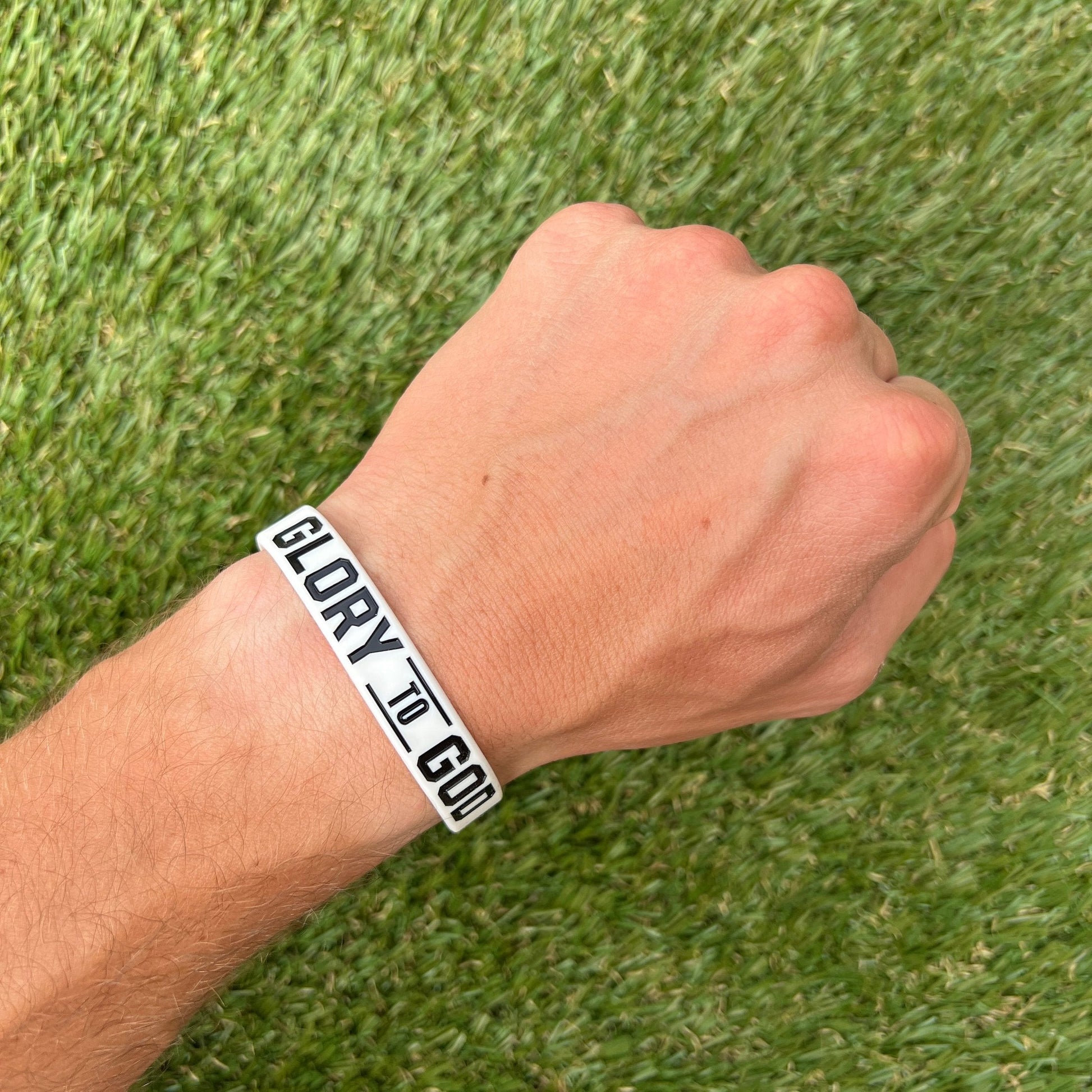 Hand wearing a 'GLORY TO GOD' bracelet on a grass background