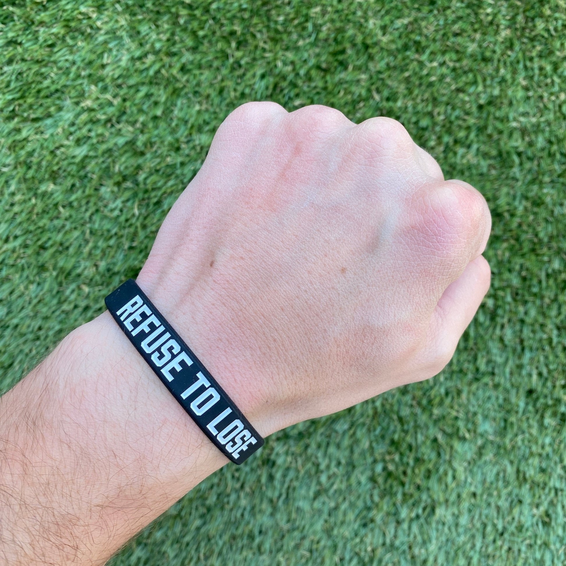 Hand wearing a black wristband with 'REFUSE TO LOSE' text on a grass background